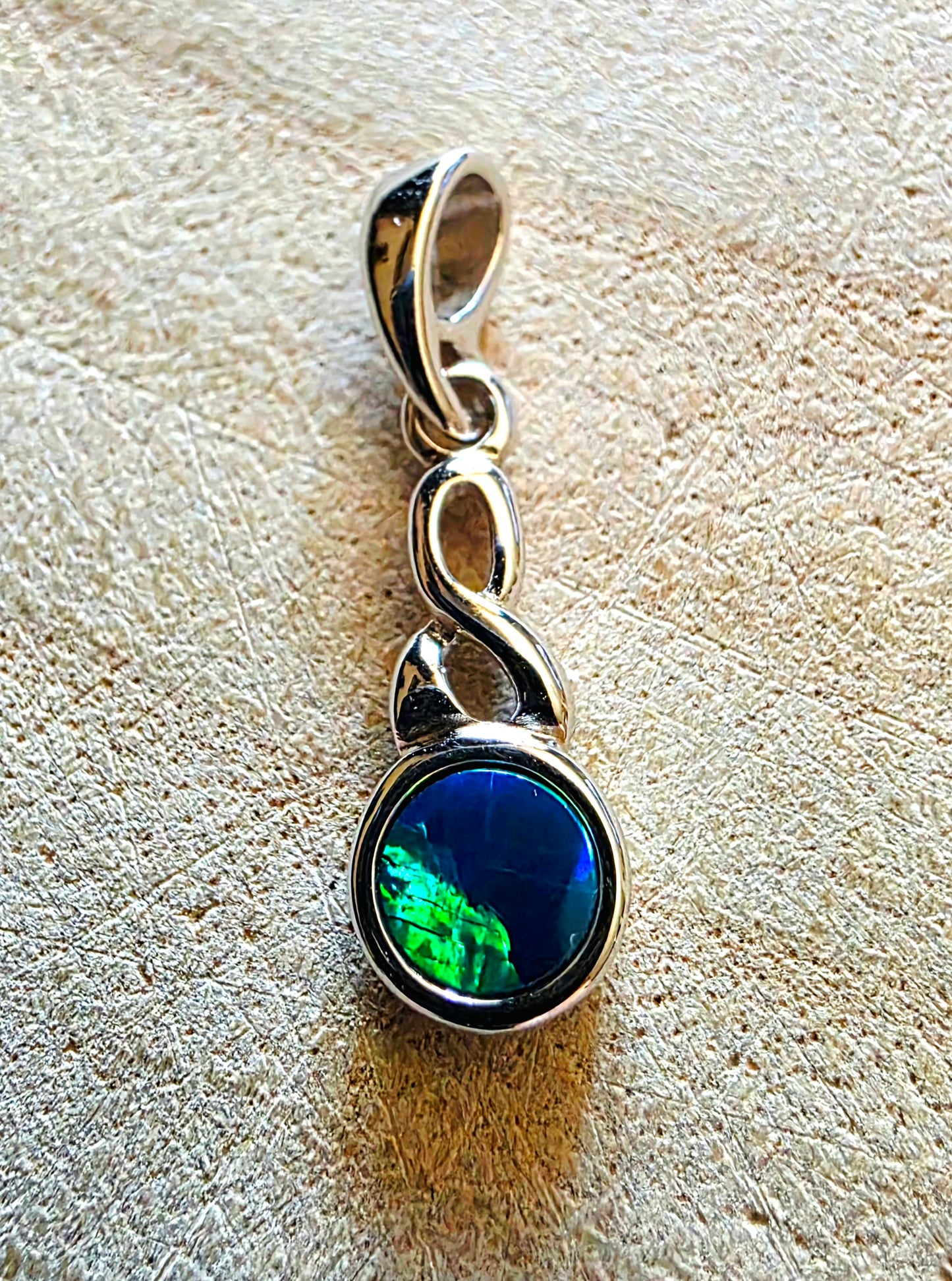 Silver pendant with a green and blue opal gemstone on a textured beige surface
