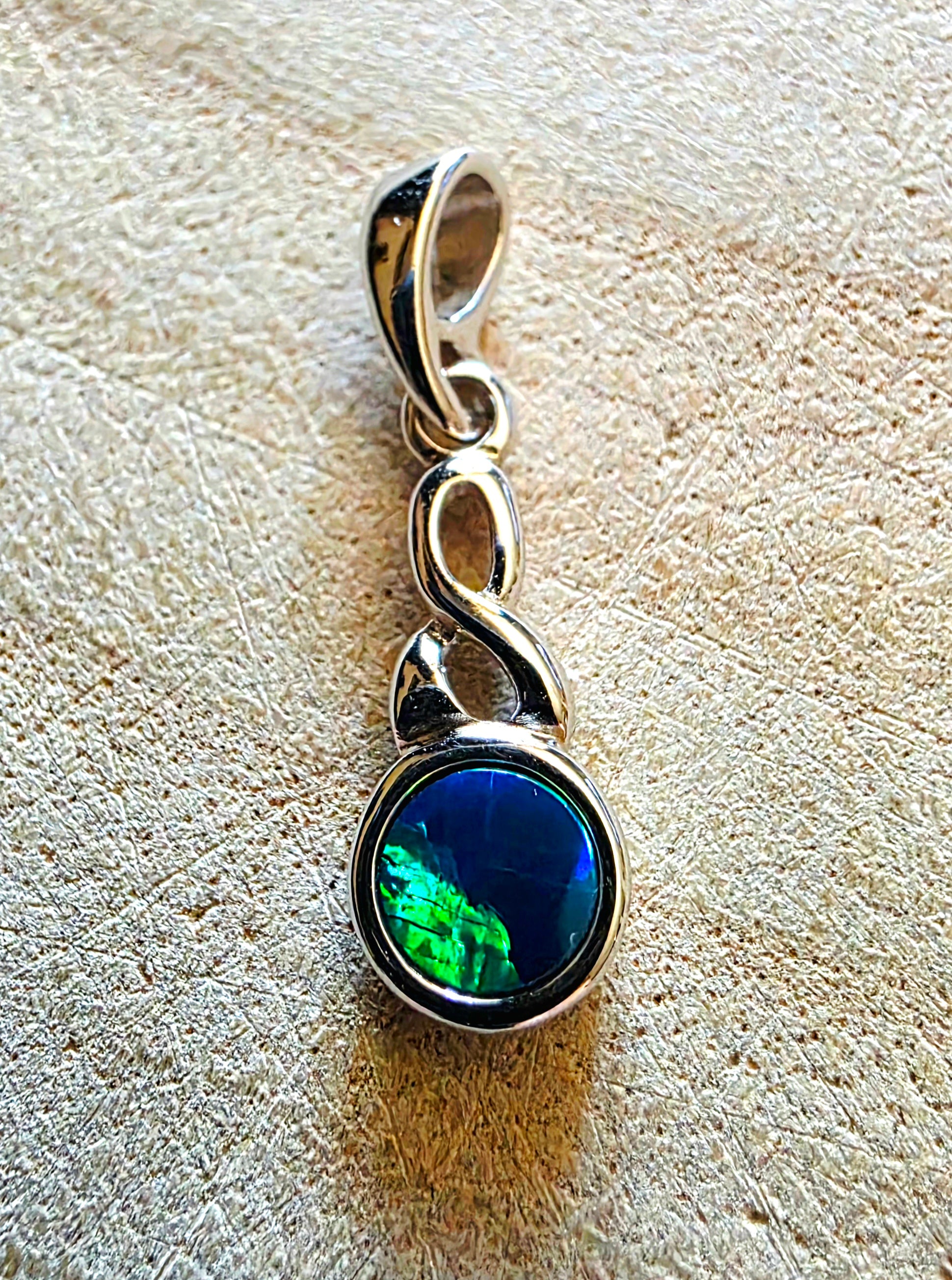 Silver pendant with a green and blue opal gemstone on a textured beige surface