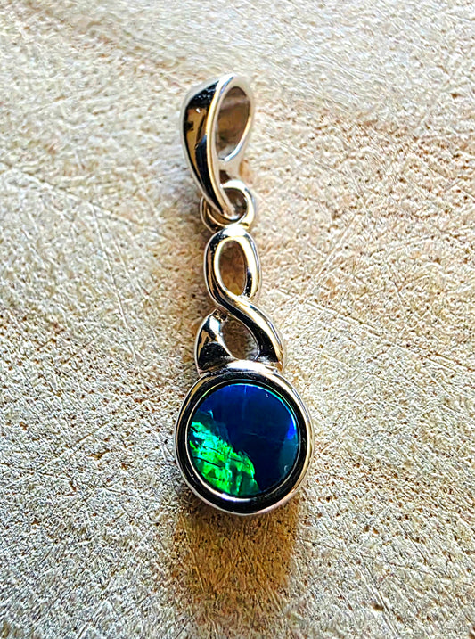 Silver pendant with a green and blue opal gemstone on a textured beige surface
