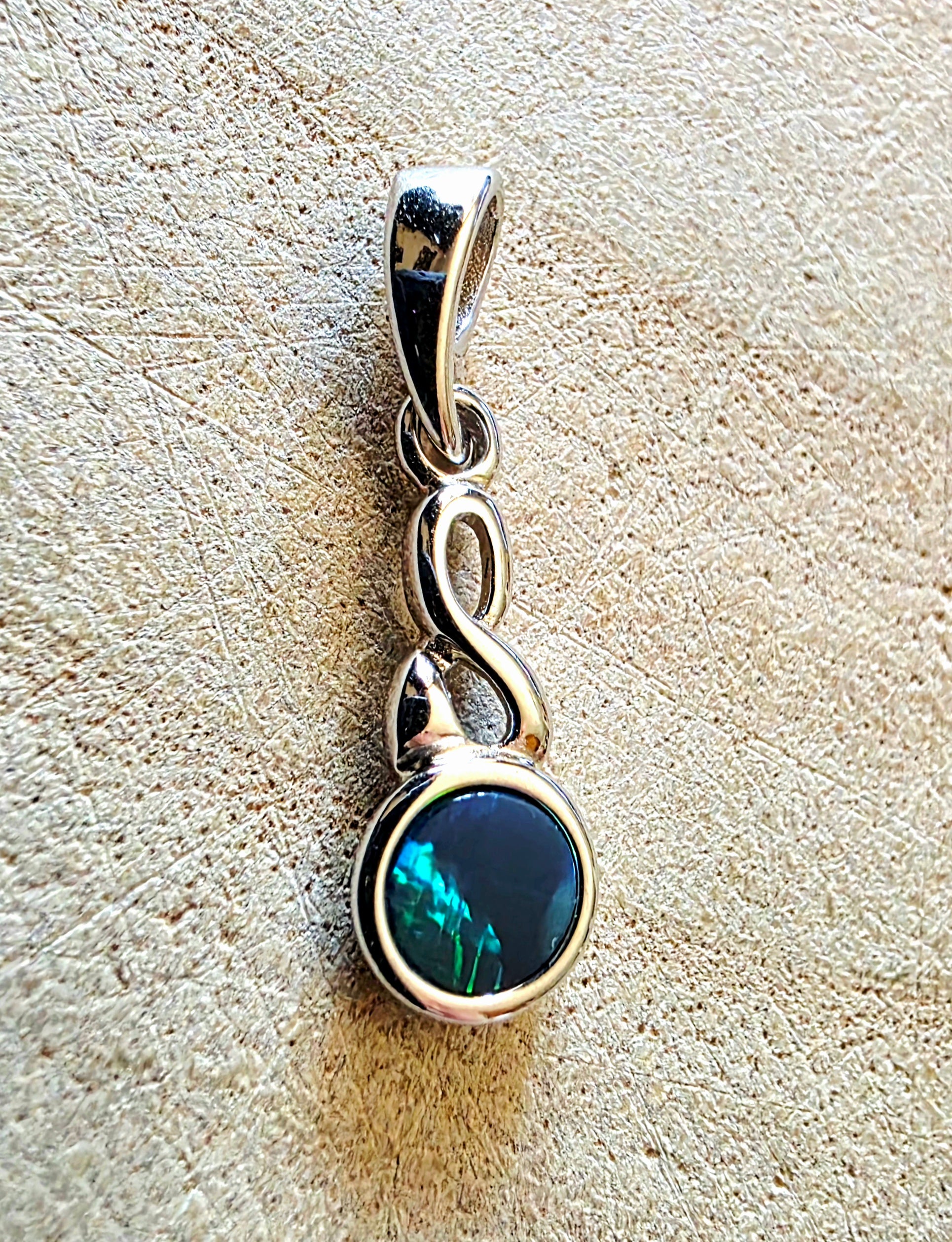 Silver pendant with a dark opal gemstone on a textured beige surface