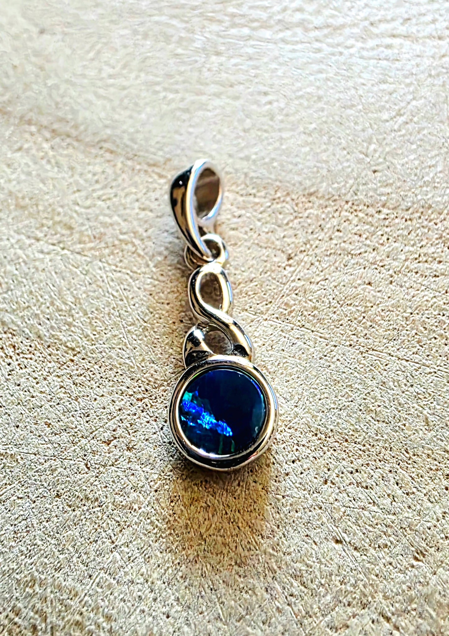 Silver pendant with a blue opal gemstone on a textured beige surface