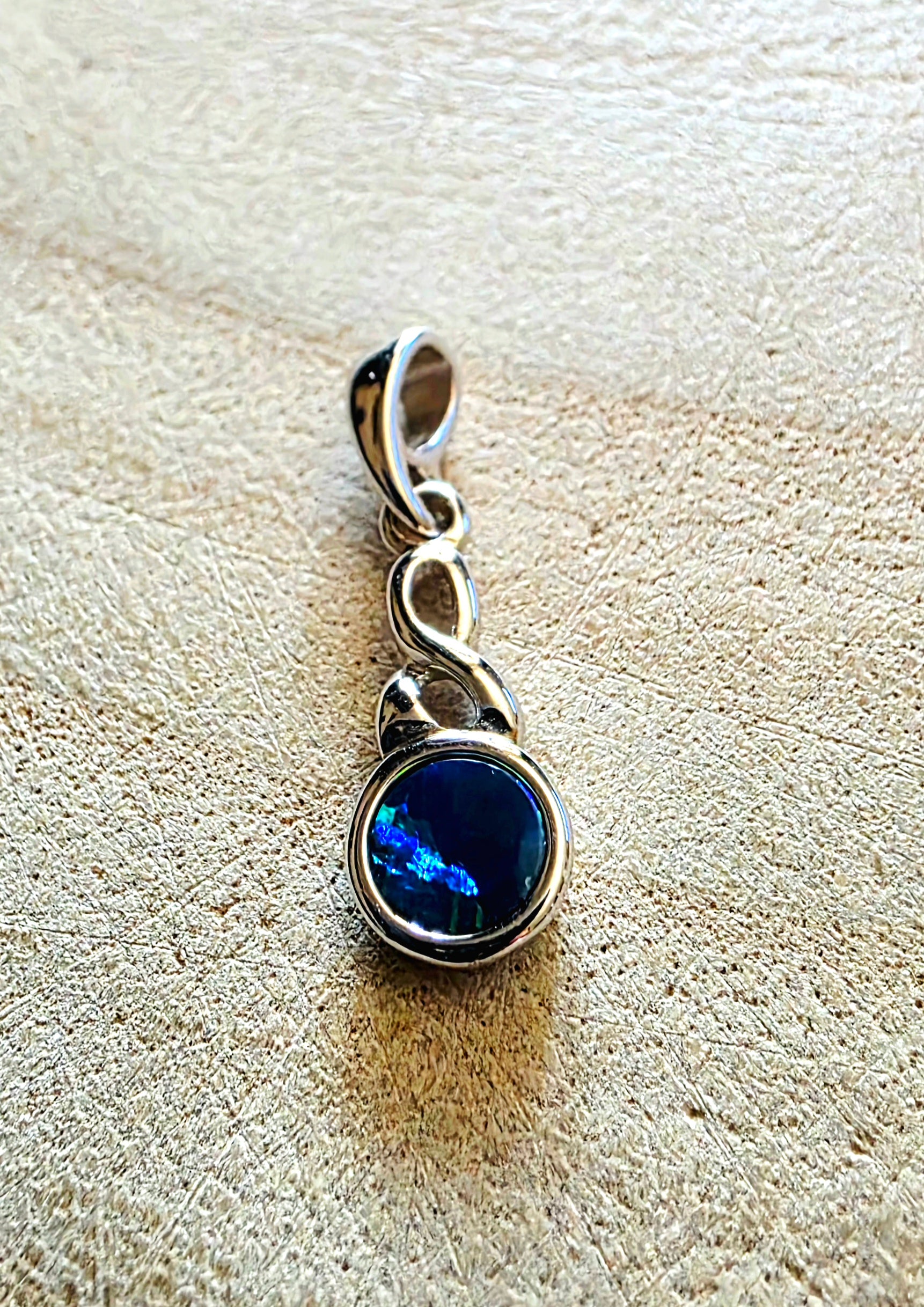 Silver pendant with a blue opal gemstone on a textured beige surface
