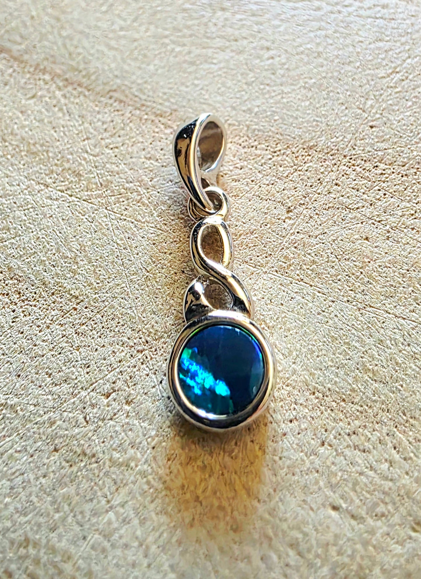 Silver pendant with a blue opal gemstone on a textured beige surface