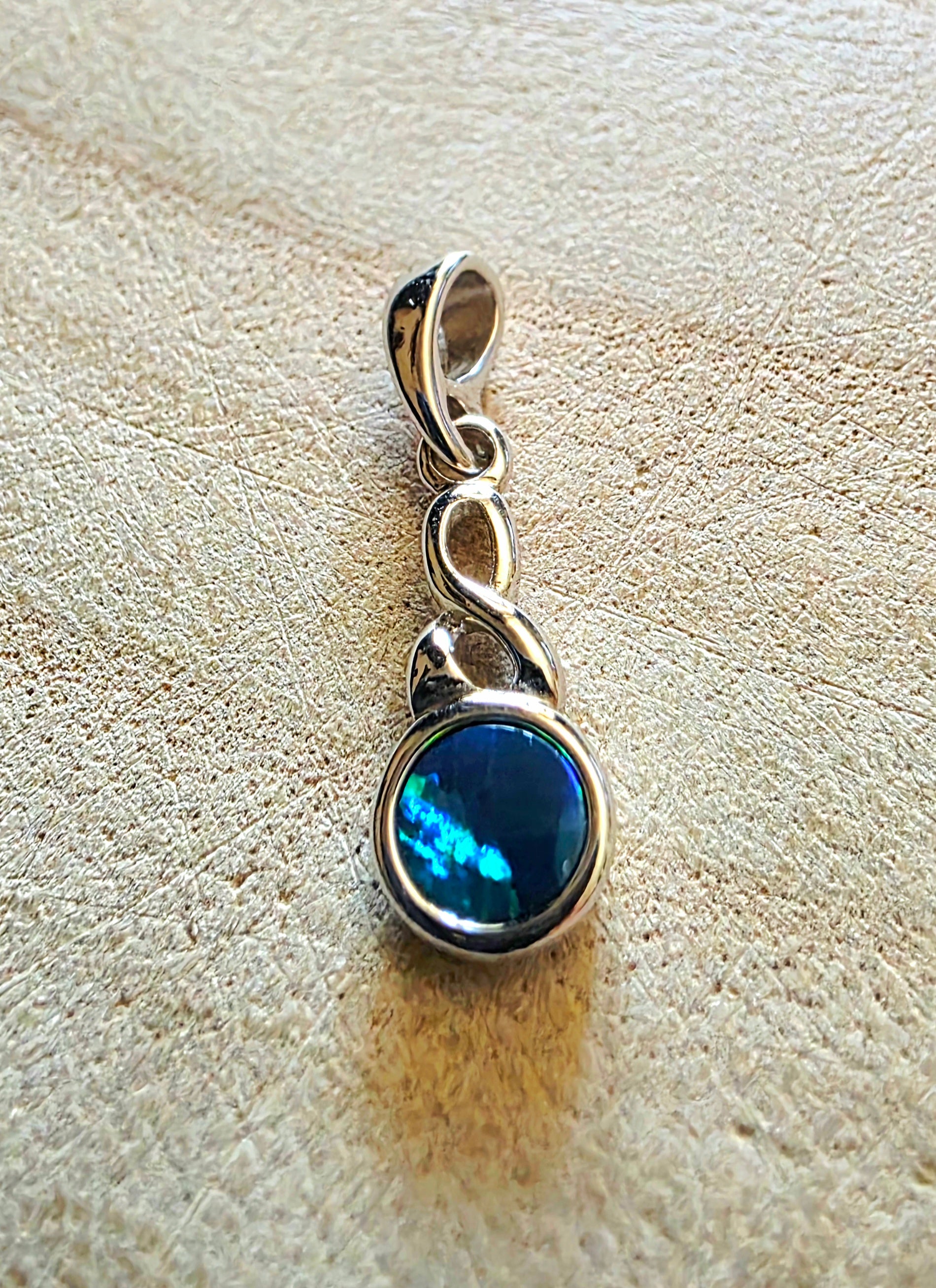 Silver pendant with a blue opal gemstone on a textured beige surface