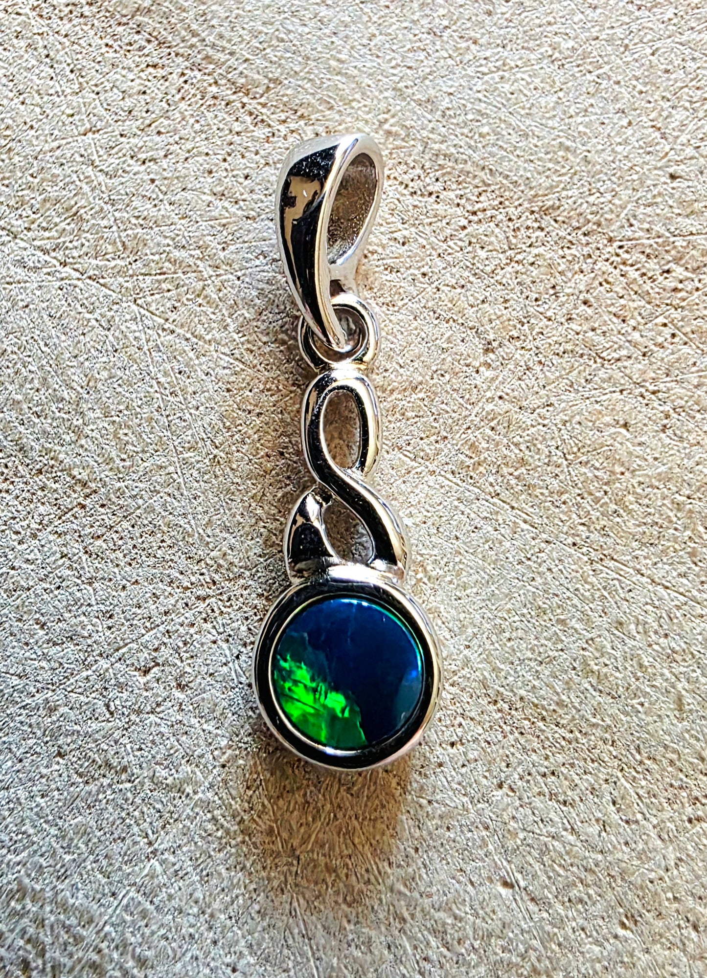 Silver pendant with a green and blue opal gemstone on a textured beige surface