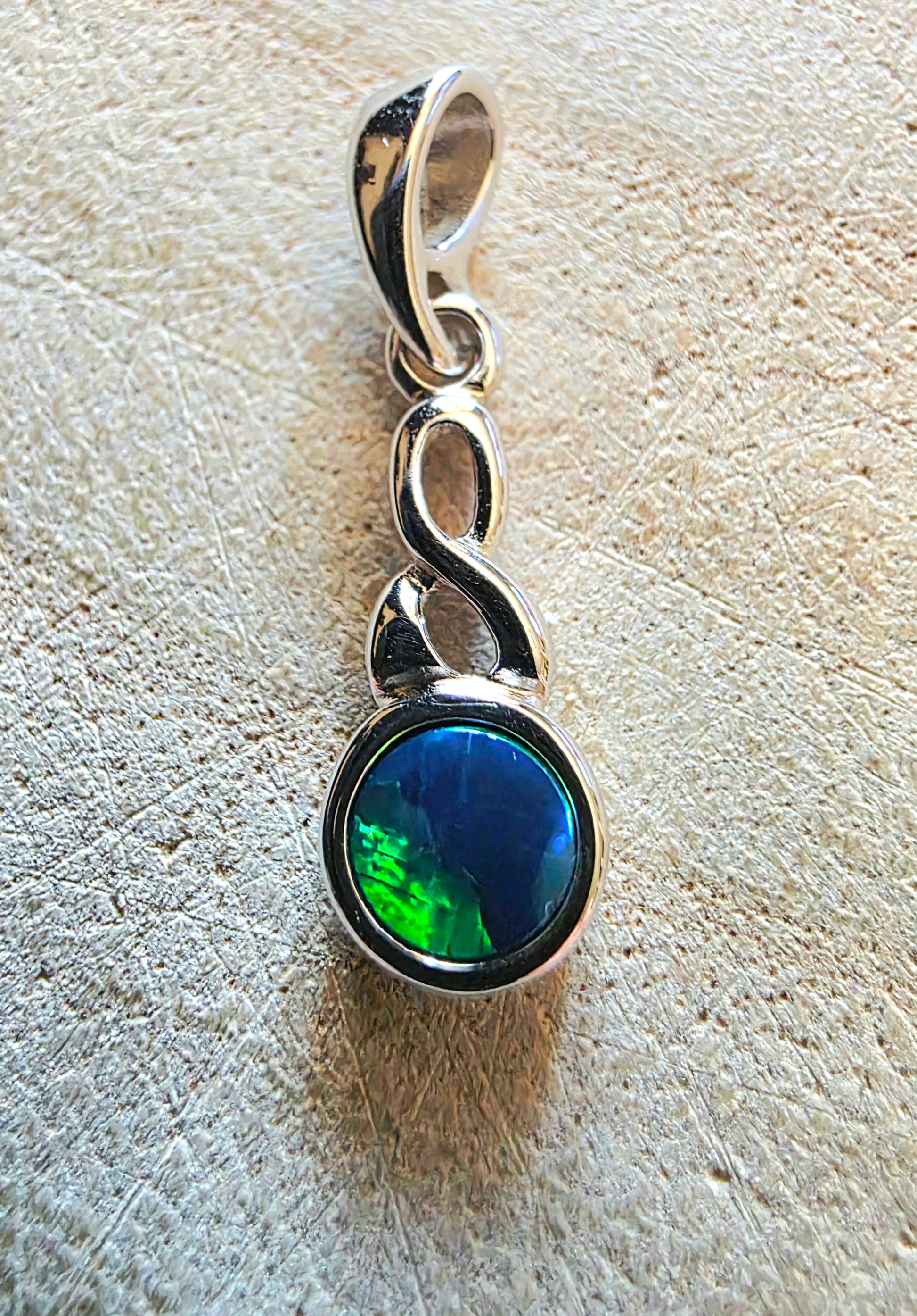 Silver pendant with a green gemstone on a textured beige surface