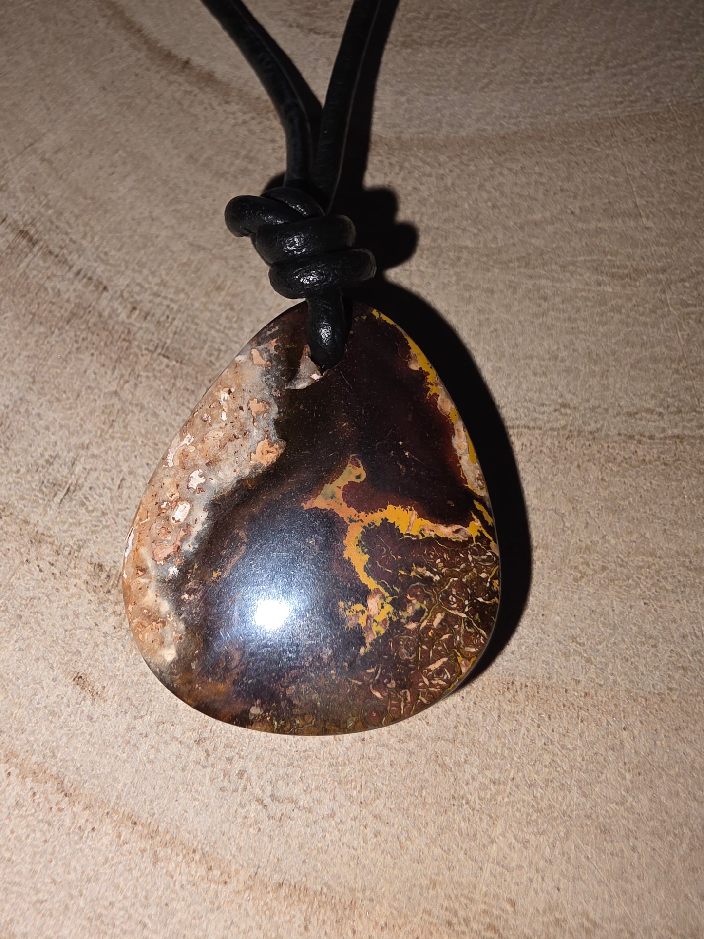 Necklace with a large, dark boulder opal pendant on a textured beige background