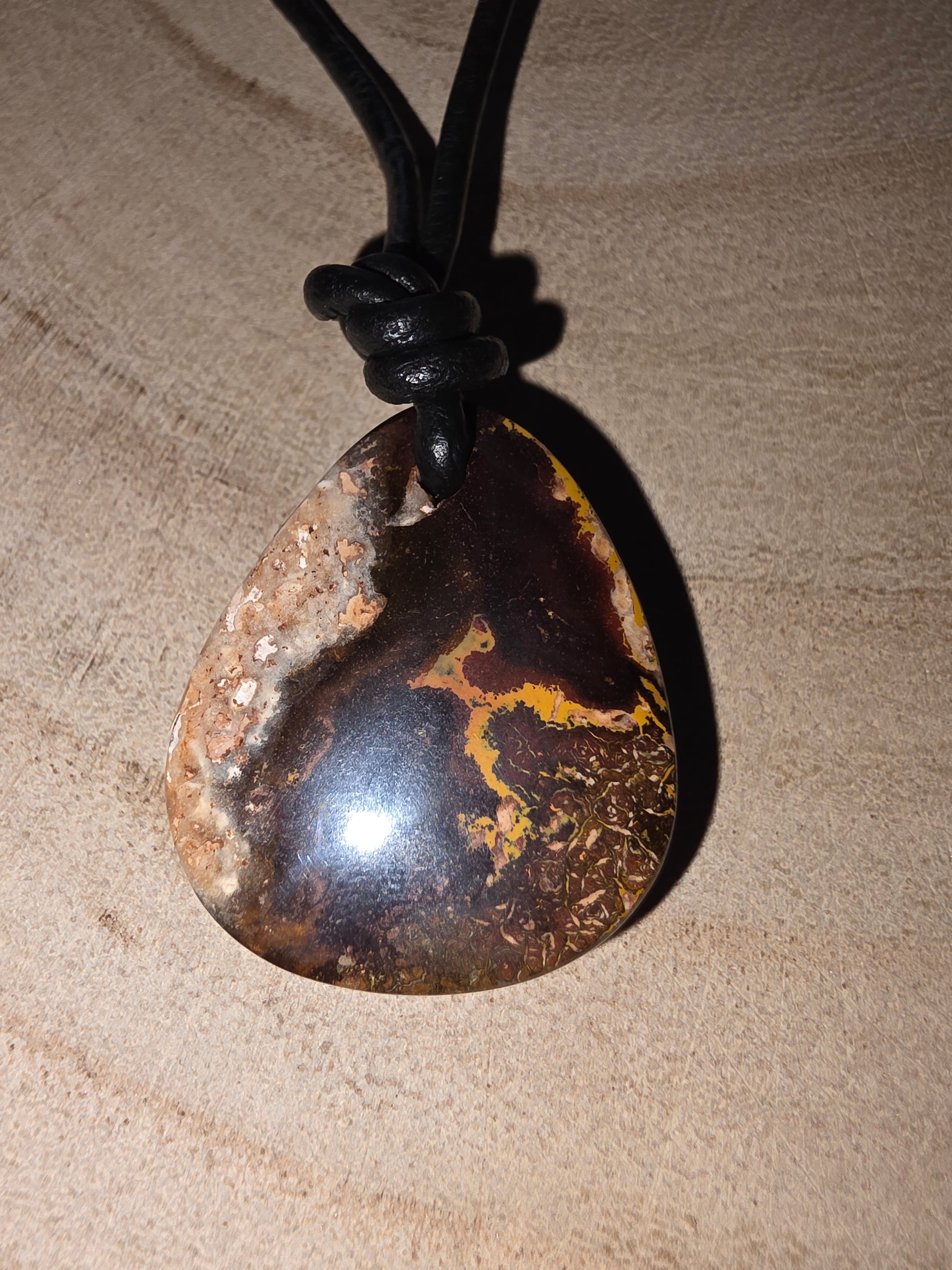 Necklace with a large, dark boulder opal pendant on a textured beige background
