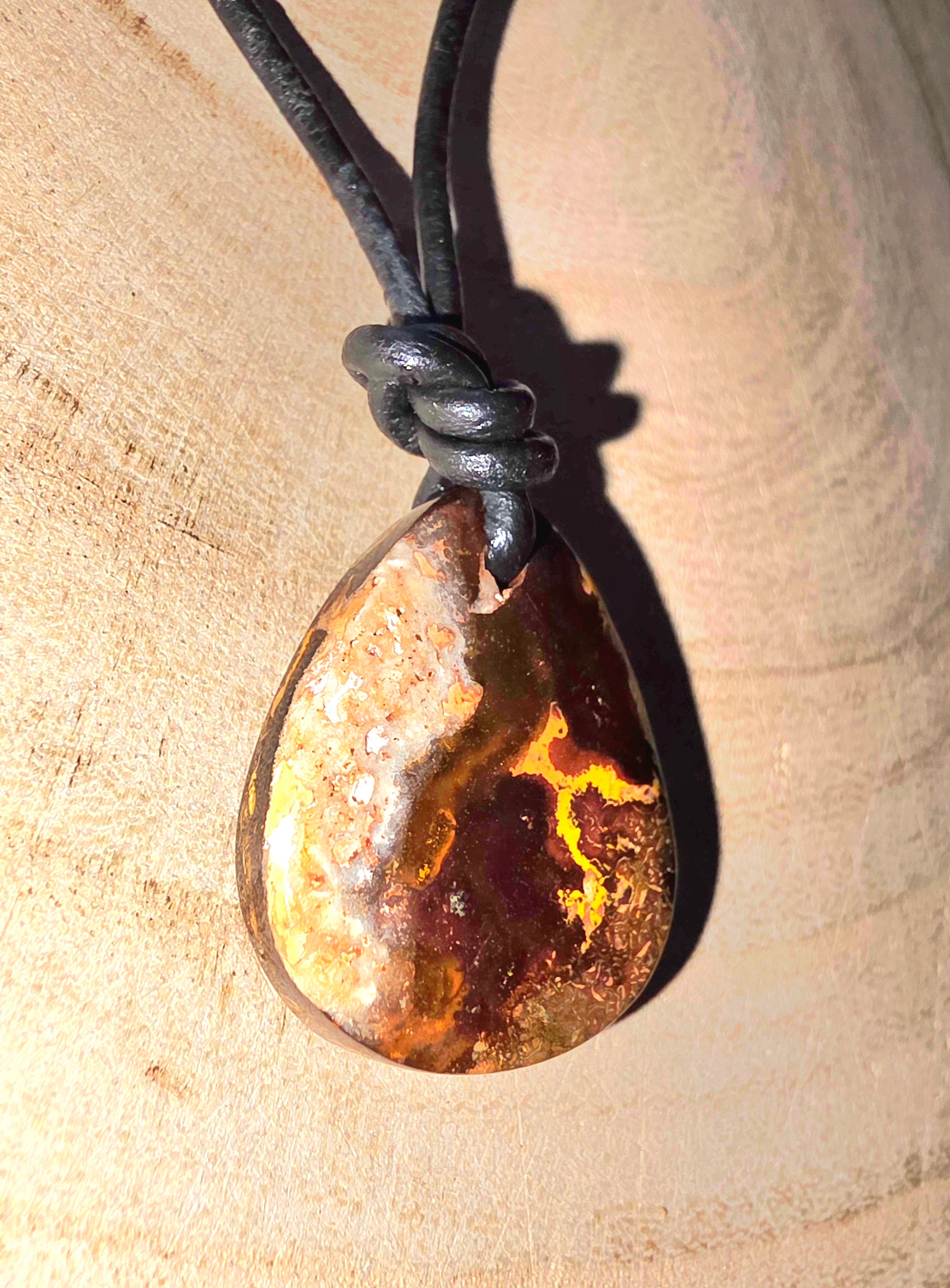 Teardrop-shaped boulder opal pendant on a black cord against a beige background