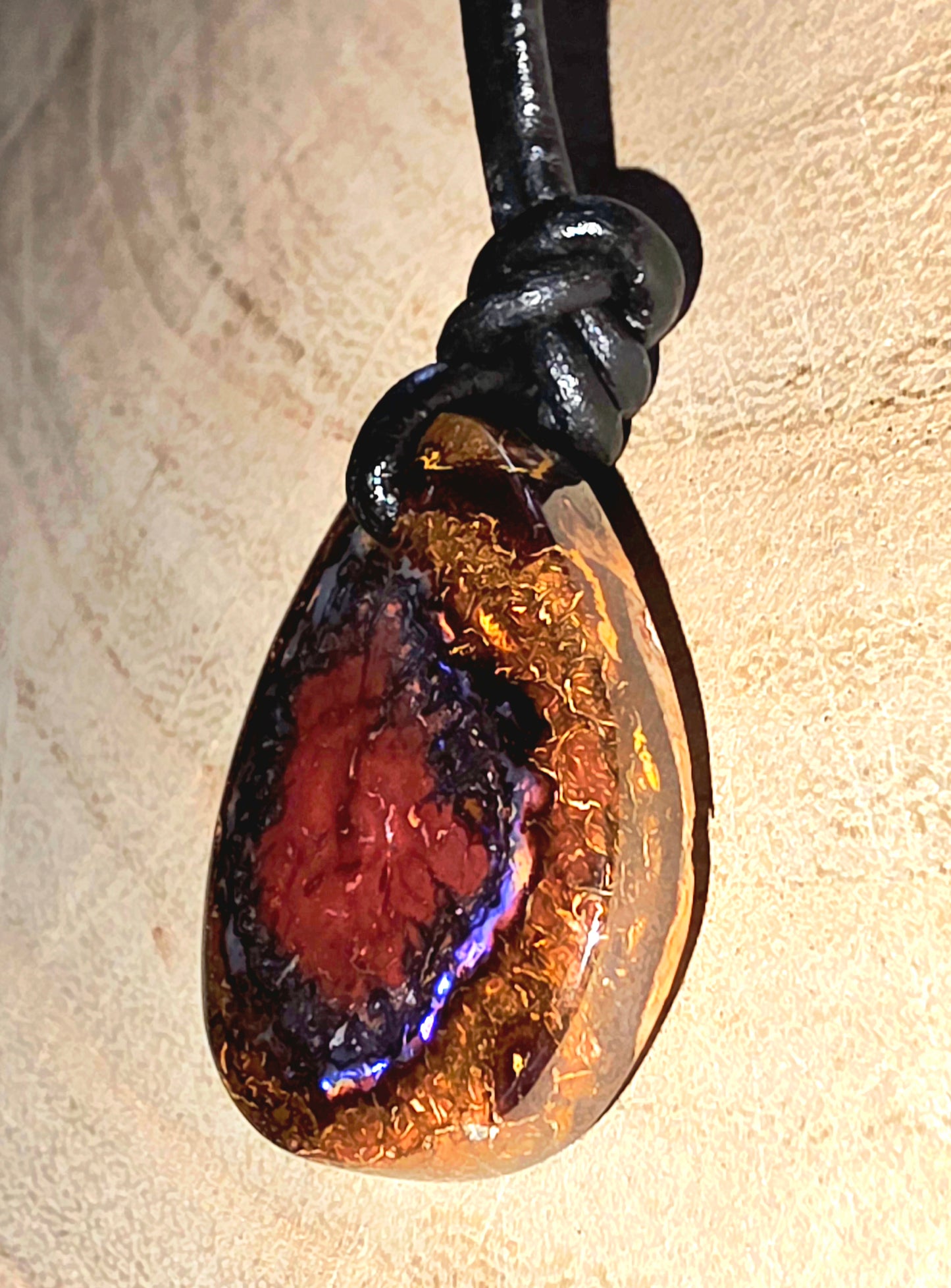 Teardrop-shaped opal pendant on a black cord against a beige background