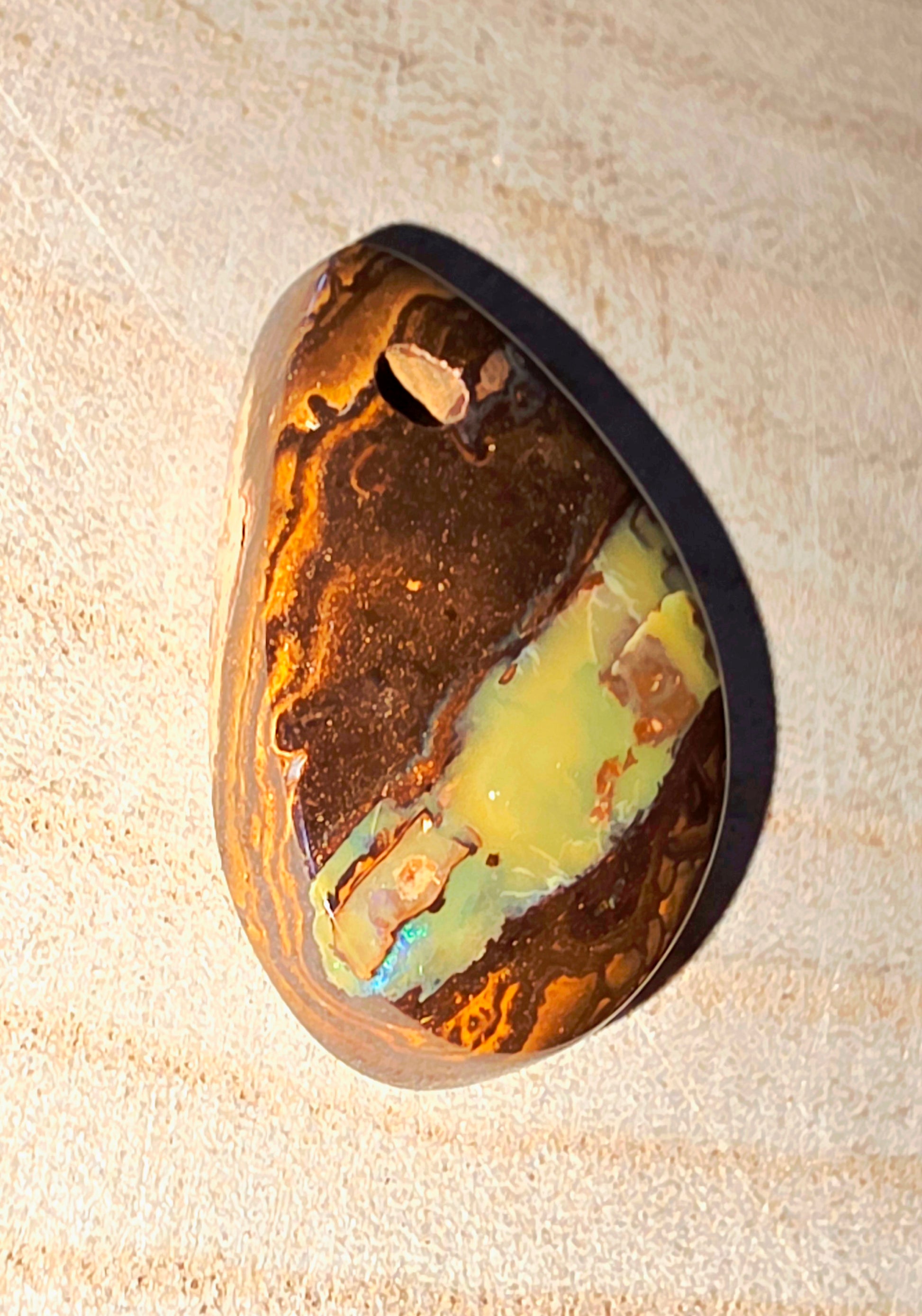 Multicoloured opal stone with brown, green, and yellow hues on a beige background