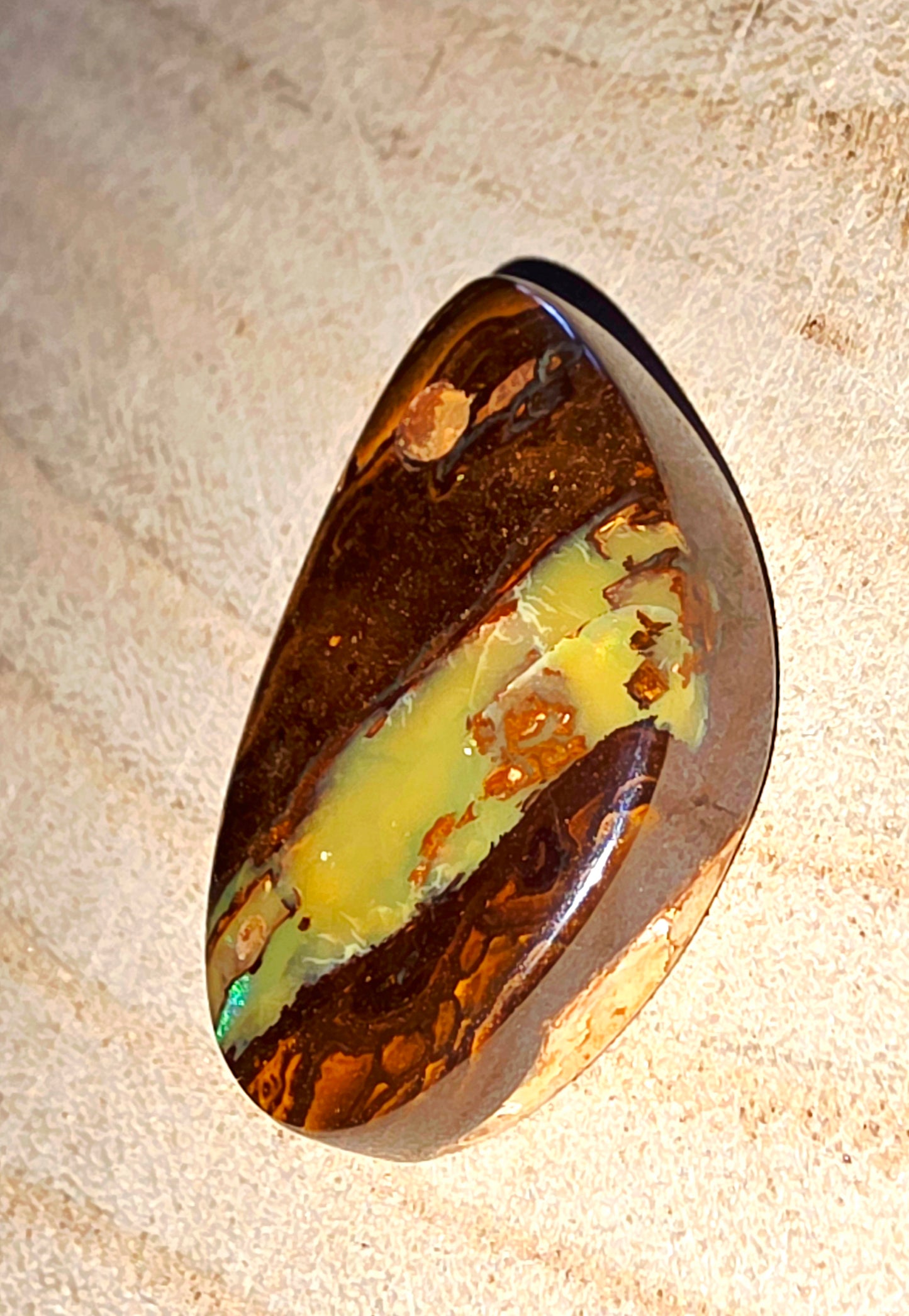 Oval-shaped opal stone with brown and yellow hues on a beige surface