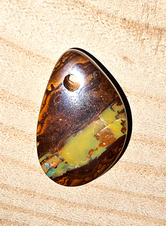 Polished opal stone with brown and green hues on a beige surface