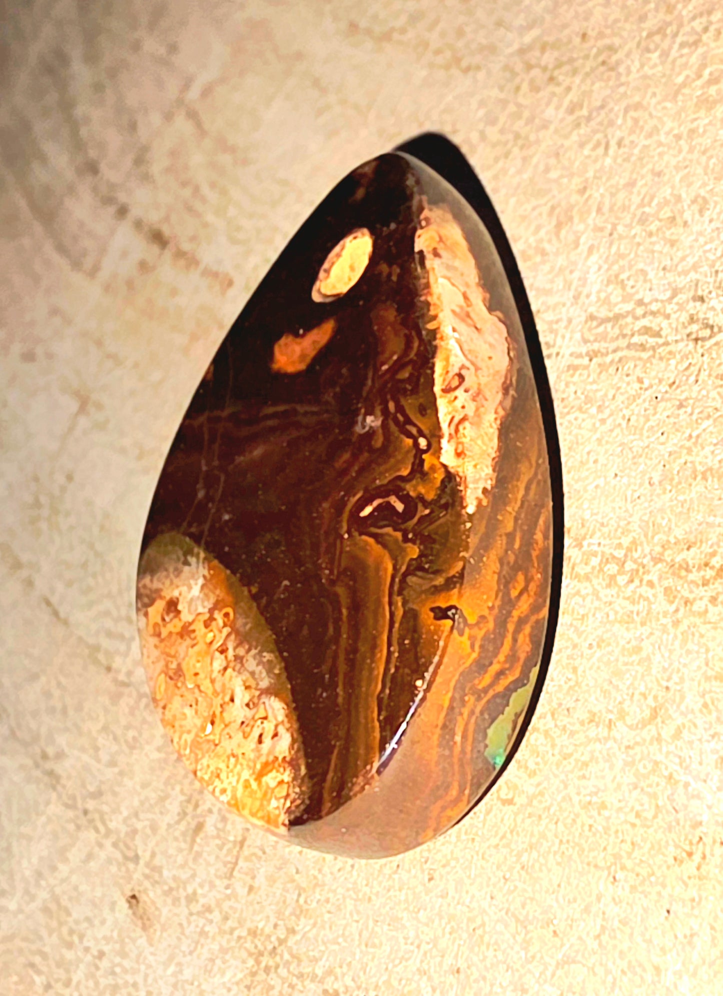 Polished opal stone with brown and gold patterns on a beige background