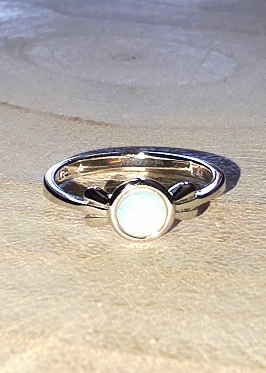 Silver ring with a white opal gemstone on a wood surface