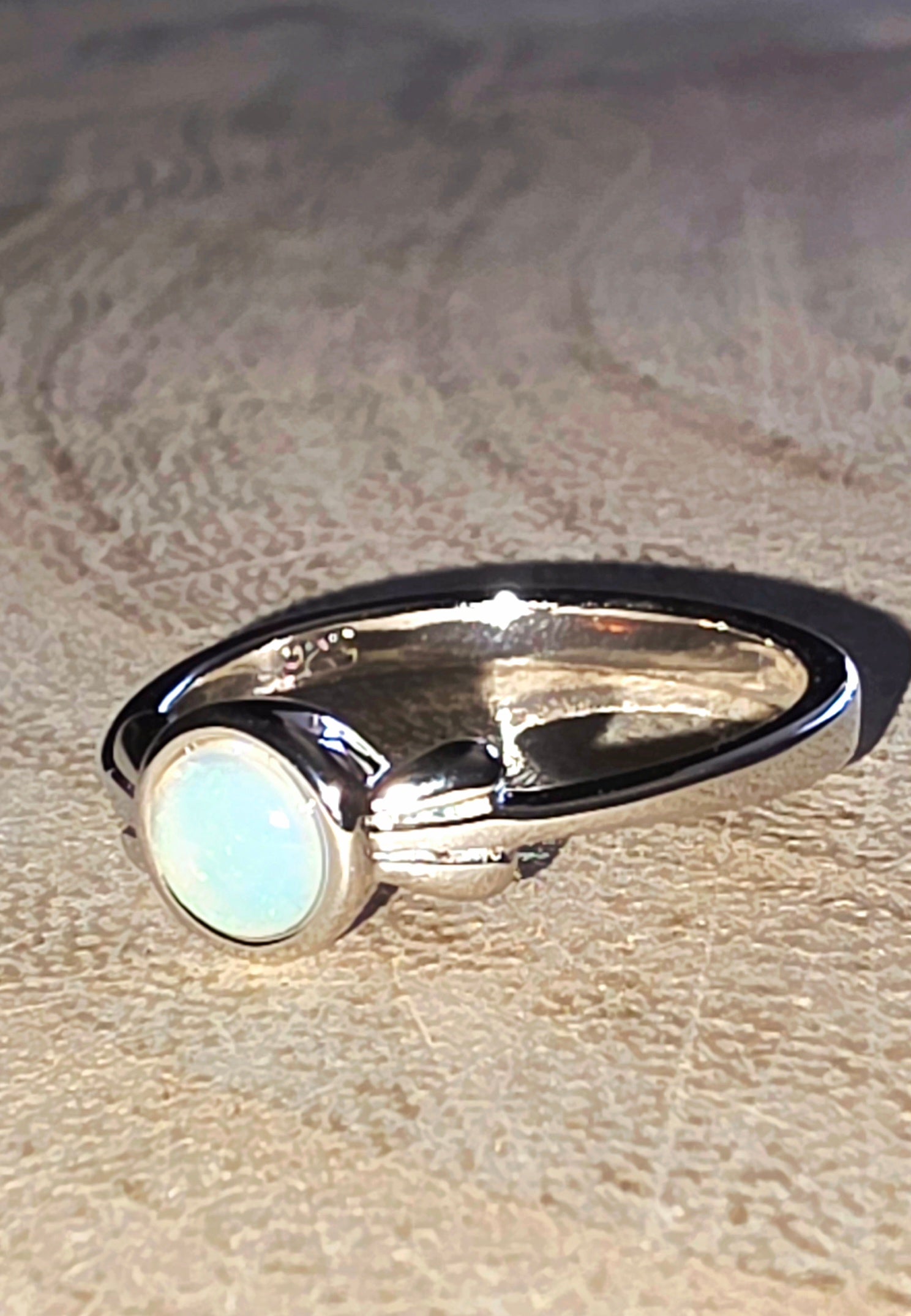 Silver ring with a circular opal gemstone on a textured beige surface