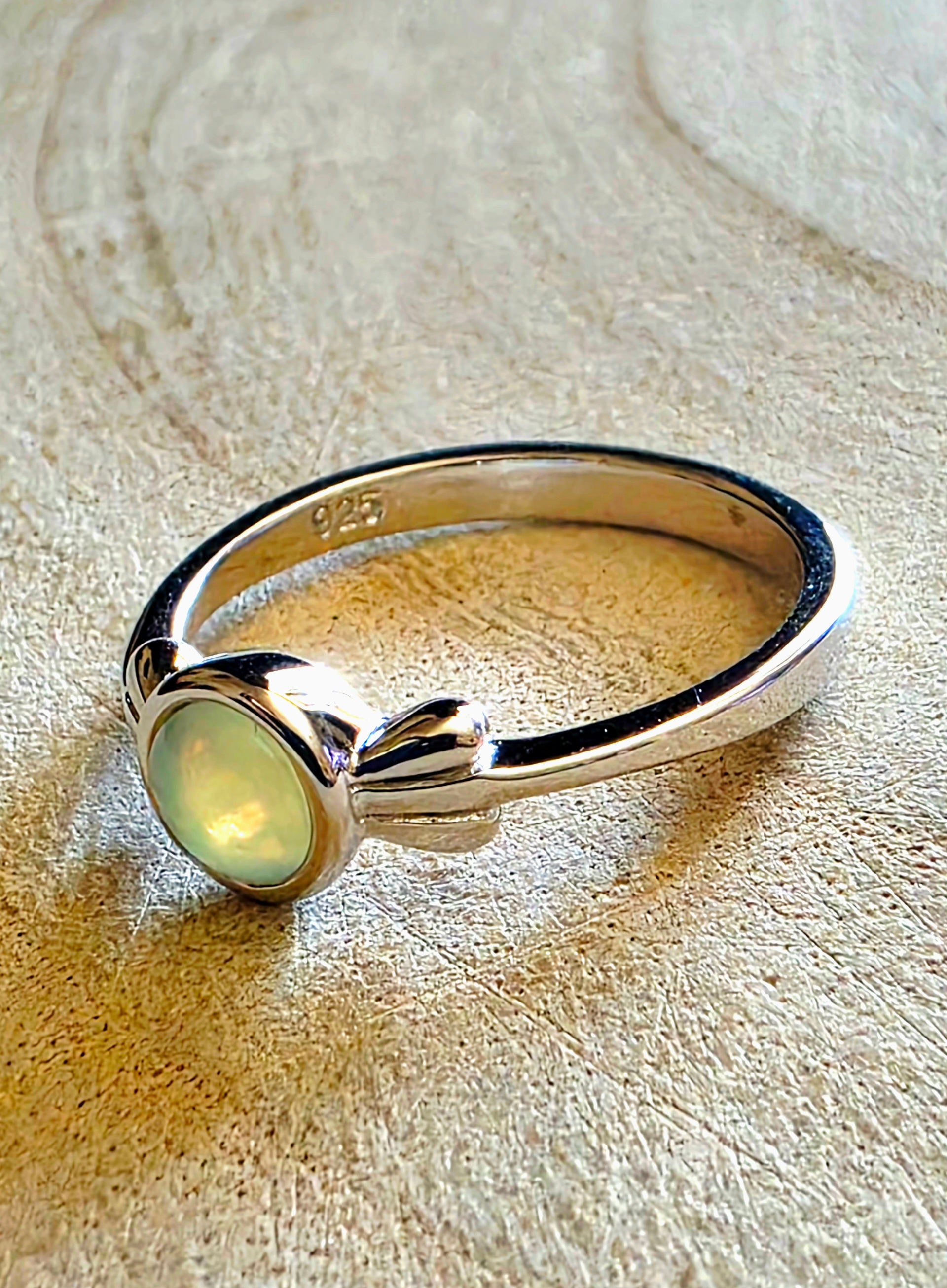 Silver ring with a central opal gemstone on a textured beige surface