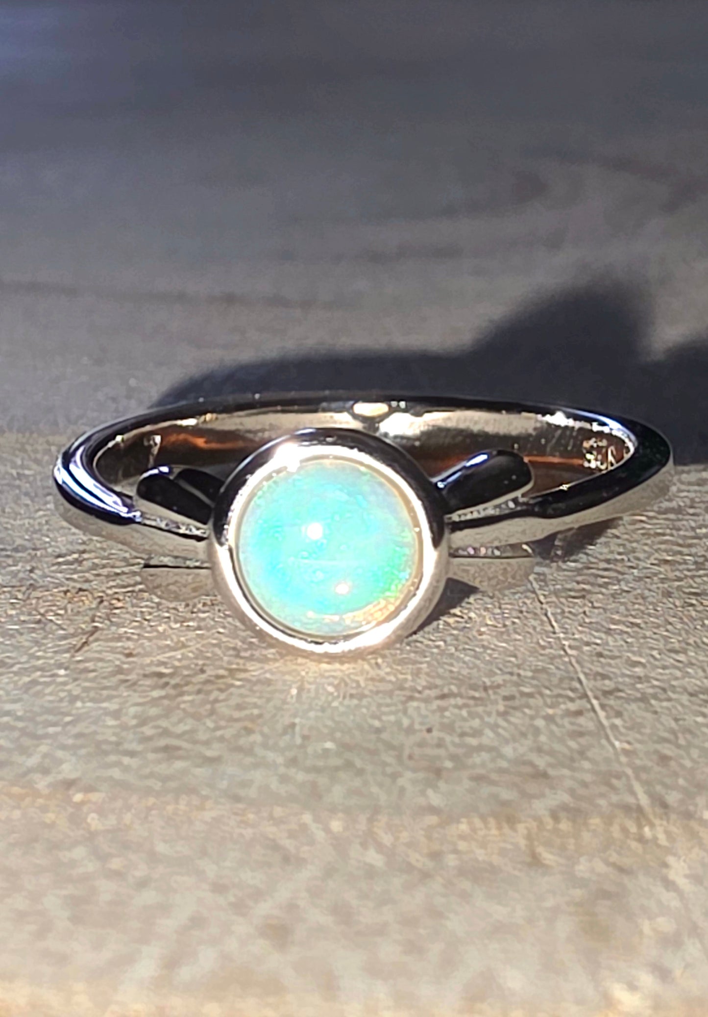 Silver ring with a central opal stone on a wood surface