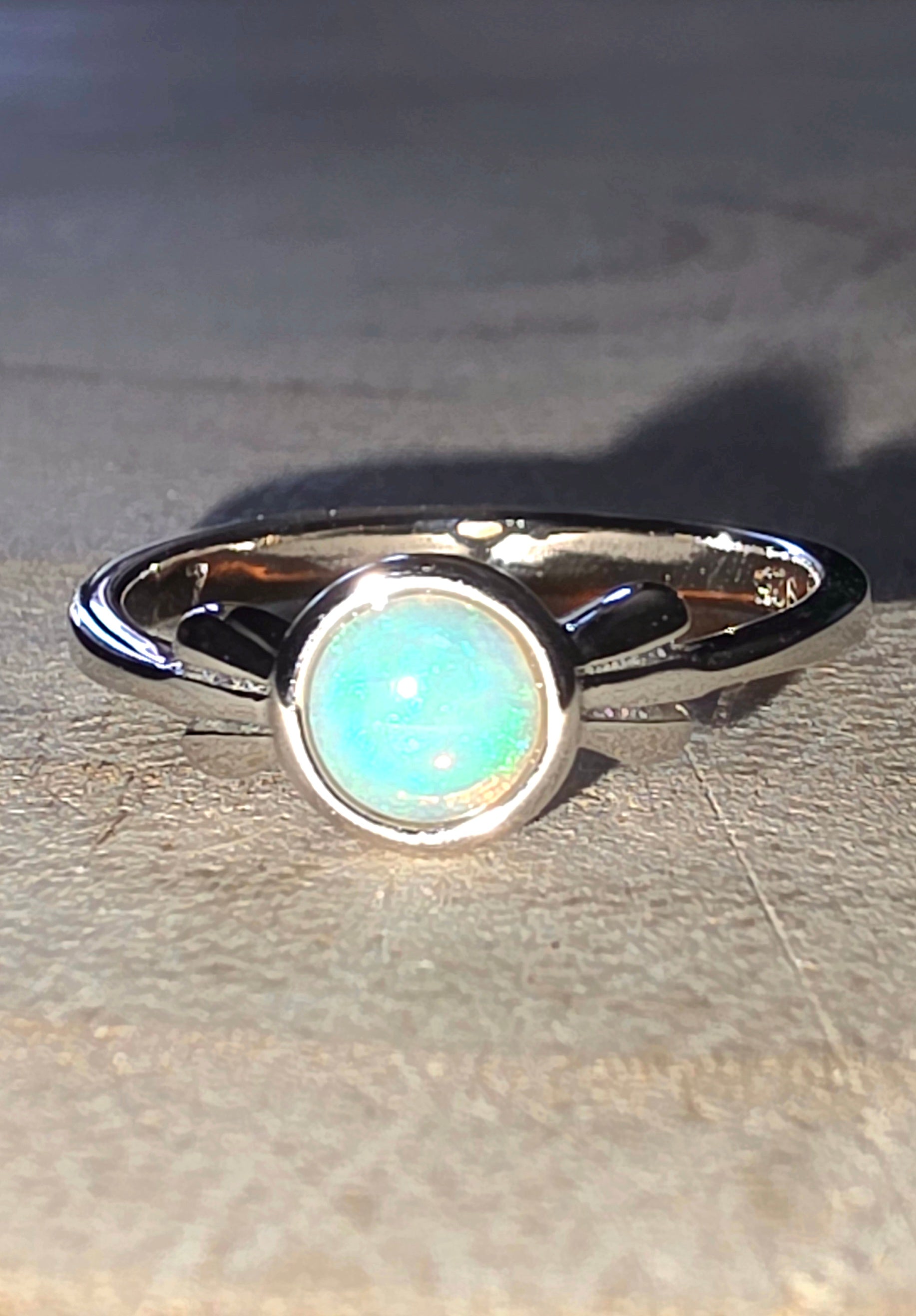 Silver ring with a central opal stone on a wood surface