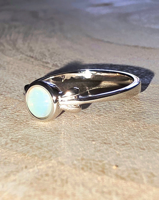 Silver ring with a round opal stone on a textured surface