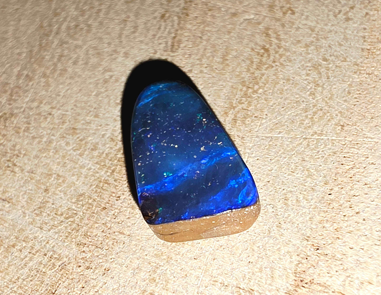 Blue black opal stone on a beige wood background