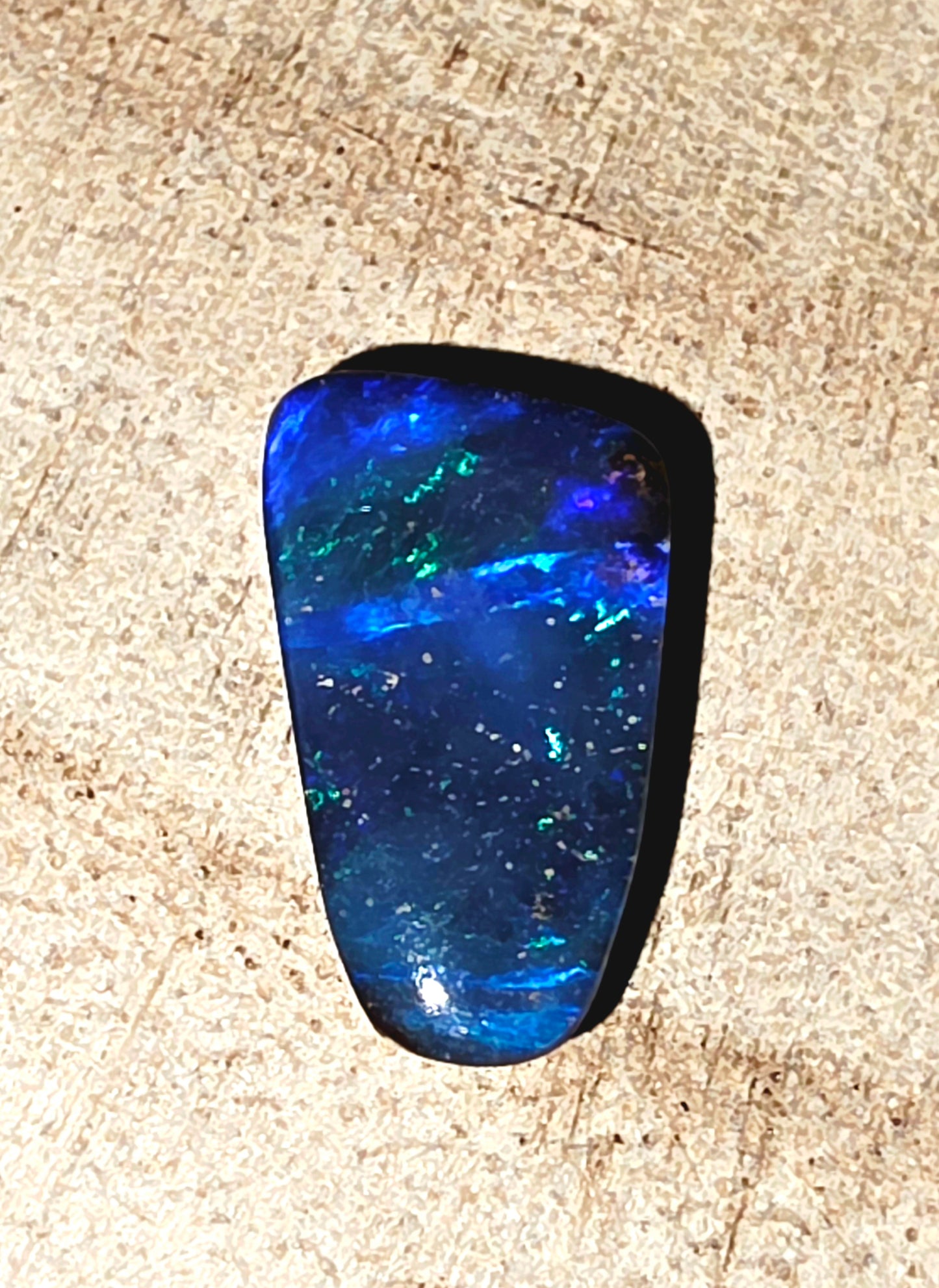 Blue black opal stone on a beige wood background