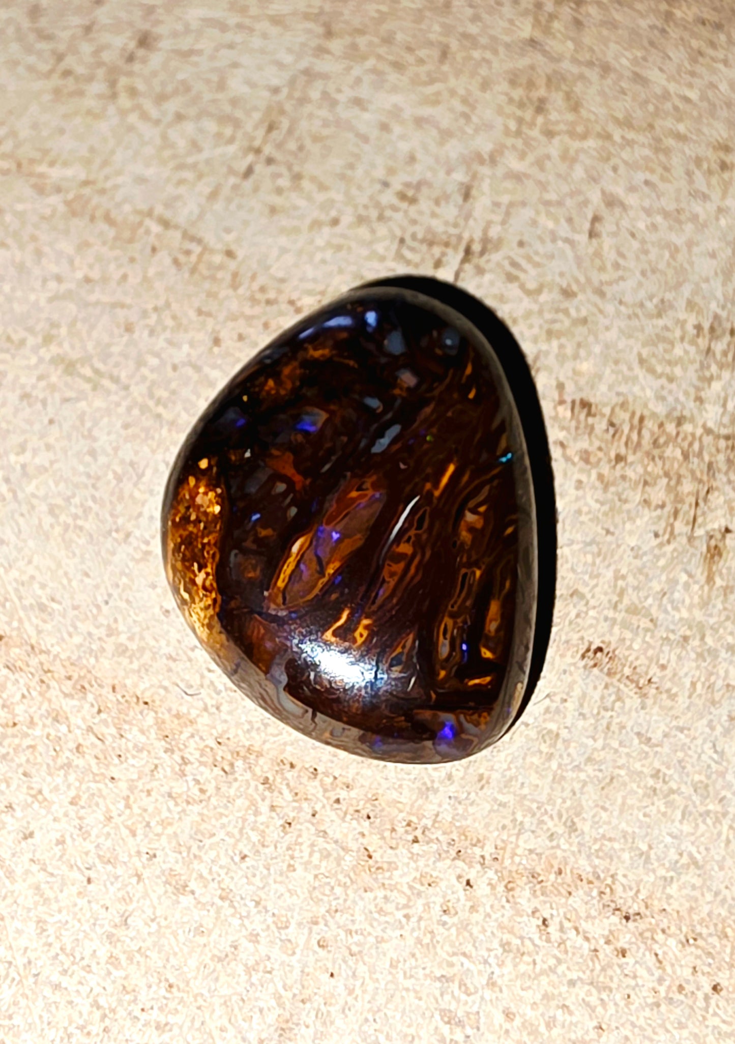 Polished boulder opal on a textured beige surface