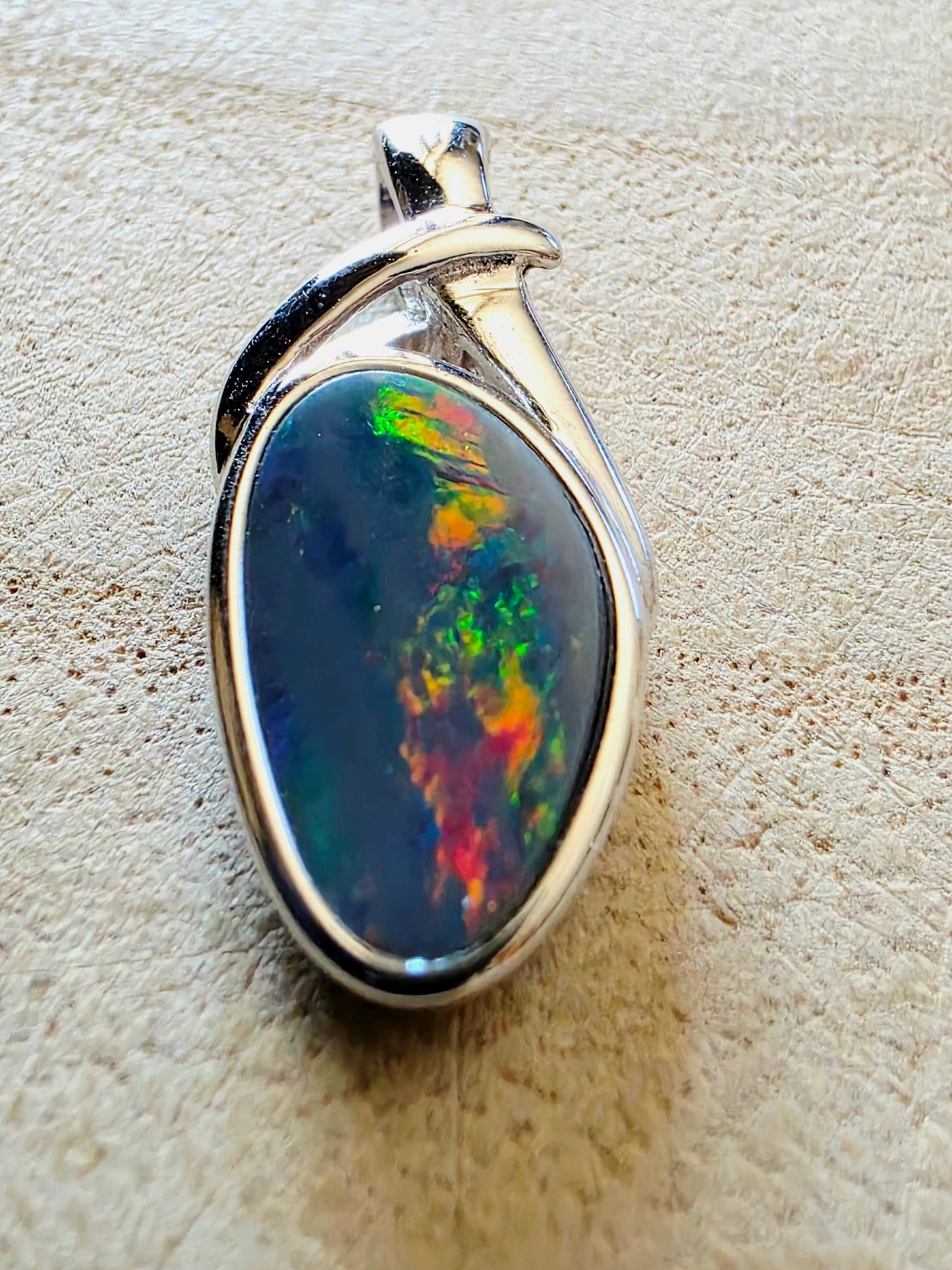 Opal pendant in a silver setting on a textured beige background