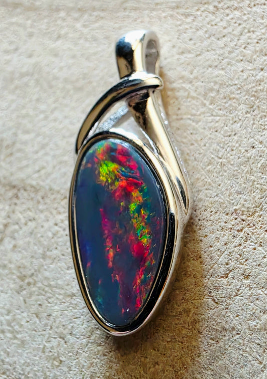 Opal pendant with a silver setting on a beige textured background