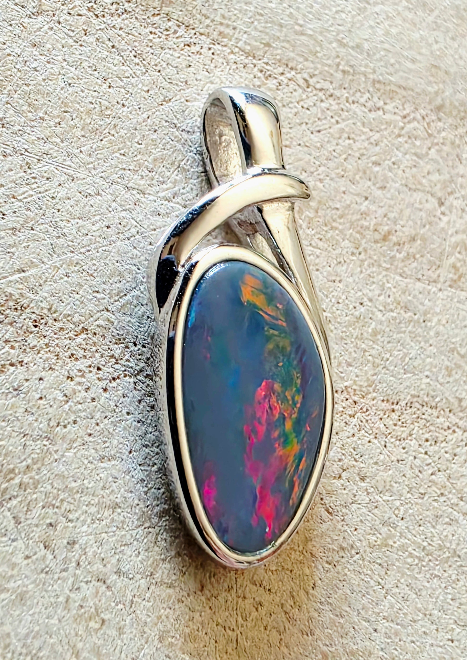 Opal pendant with silver setting on a textured beige background