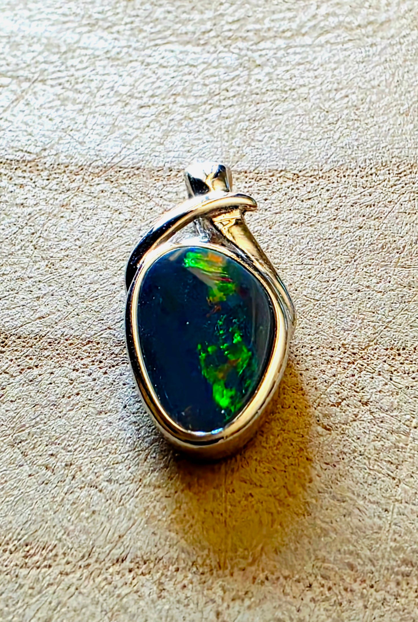 Opal pendant with silver setting on a textured beige surface