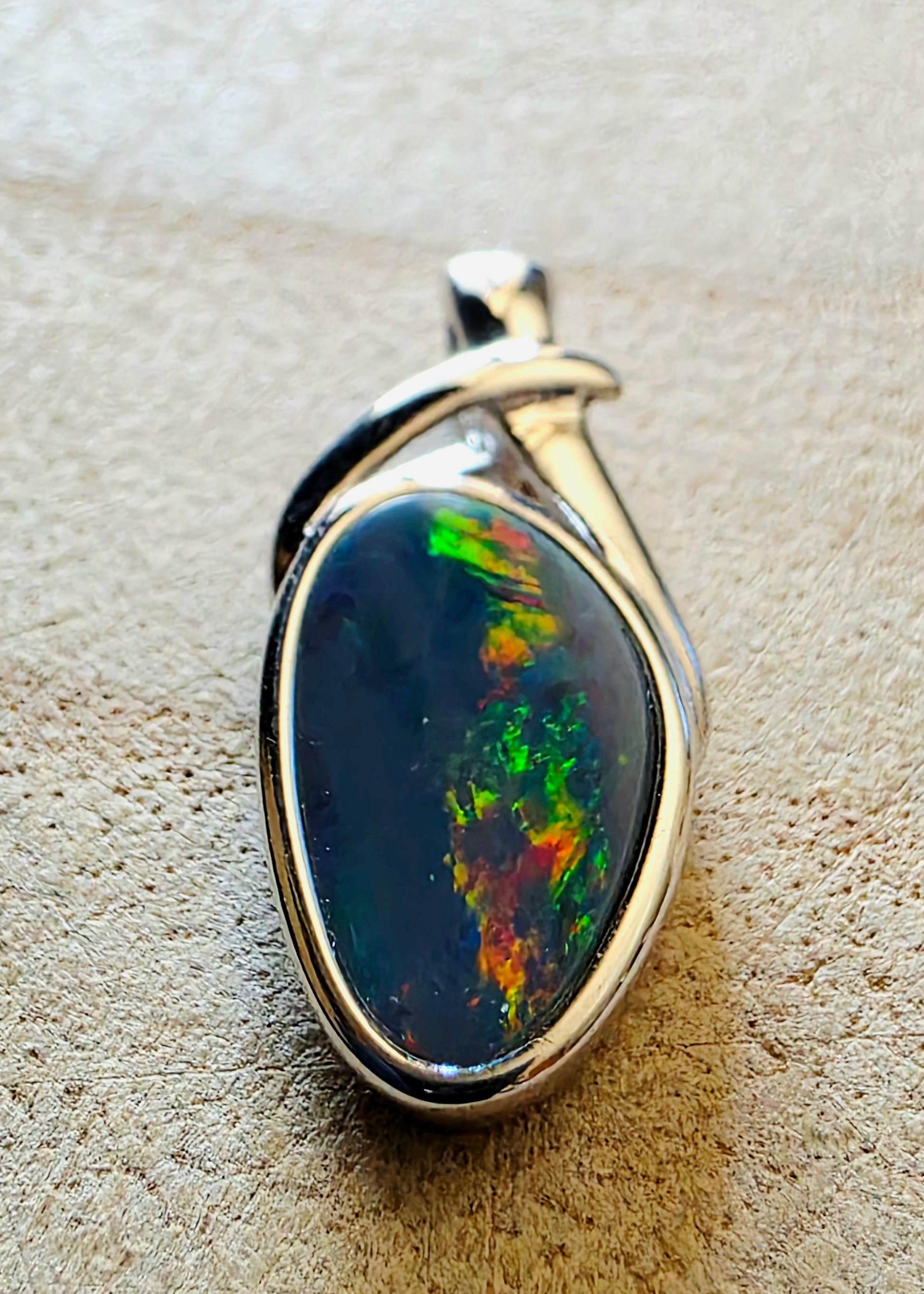 Opal pendant with silver setting on a textured beige surface
