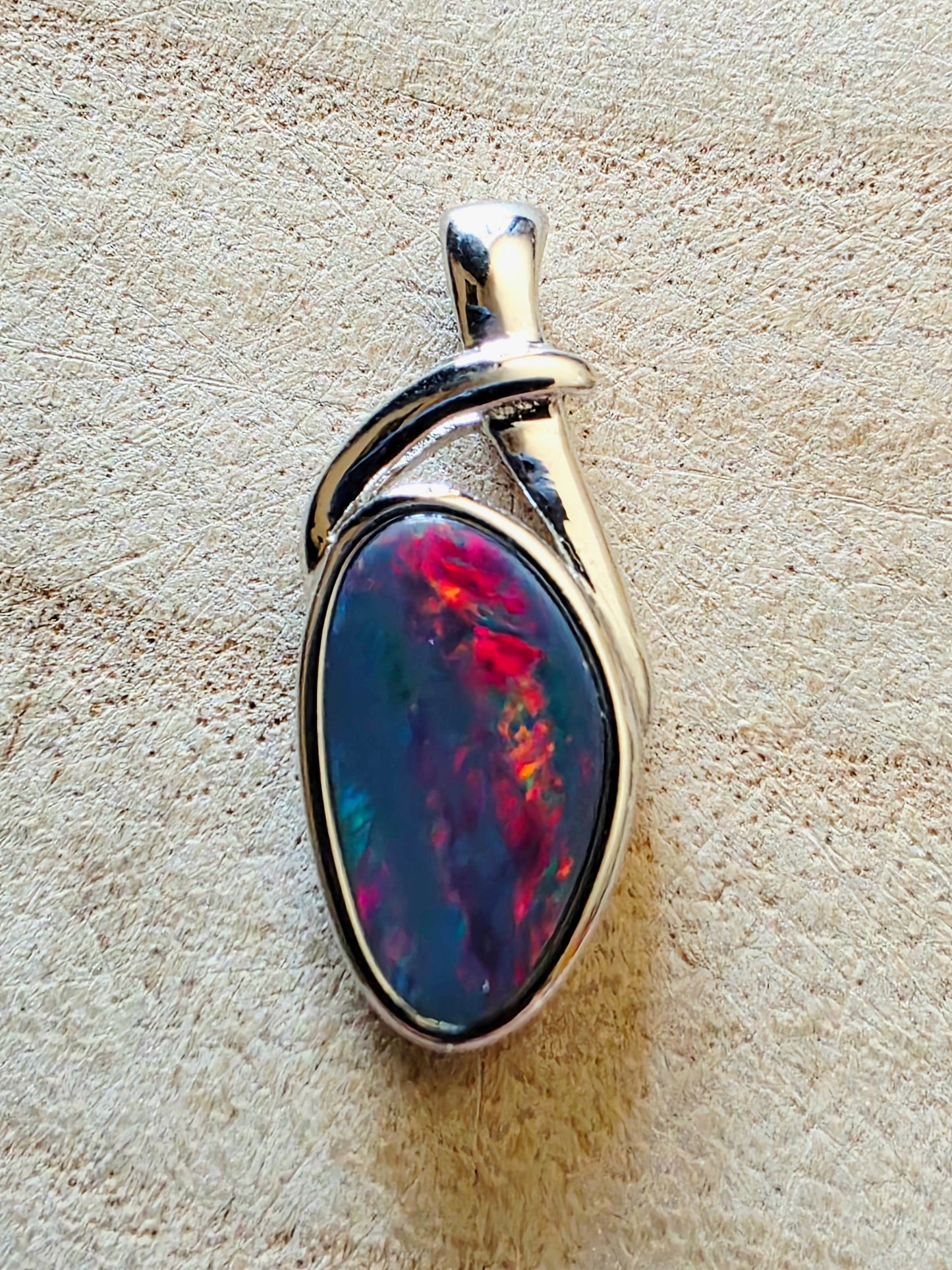 Opal pendant with silver setting on a beige stone background