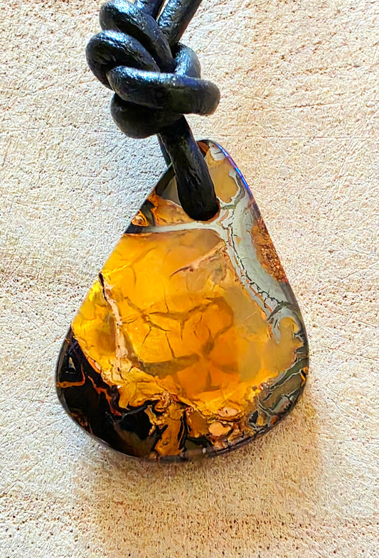 Teardrop-shaped pendant on a black cord against a beige background