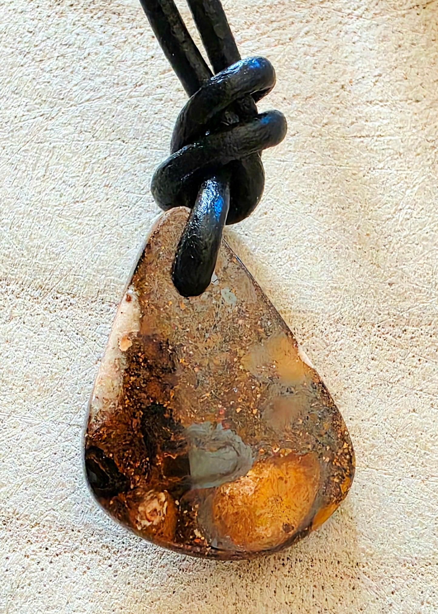 Teardrop-shaped opal pendant on a black cord against a beige background