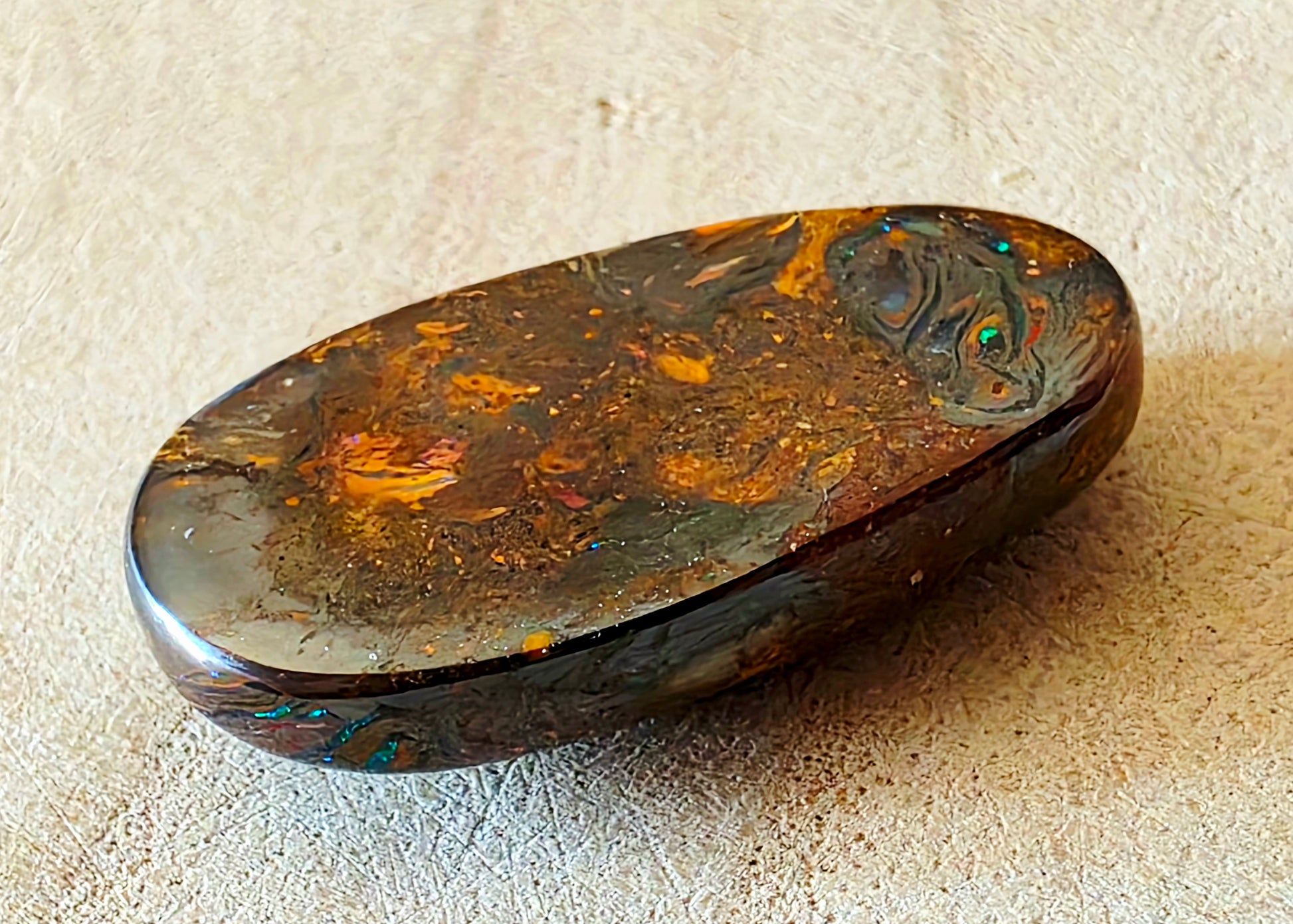 Polished opal stone with natural patterns on a beige surface