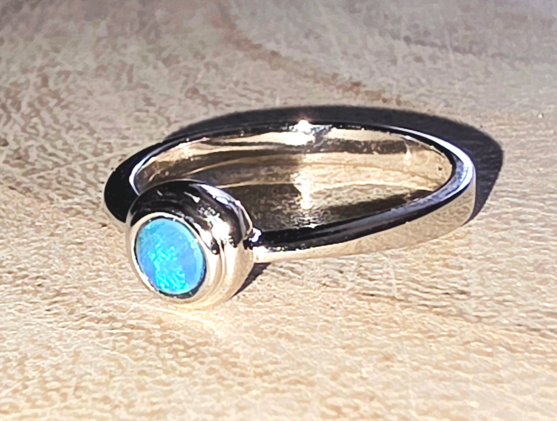 Silver ring with a blue opal on a beige surface