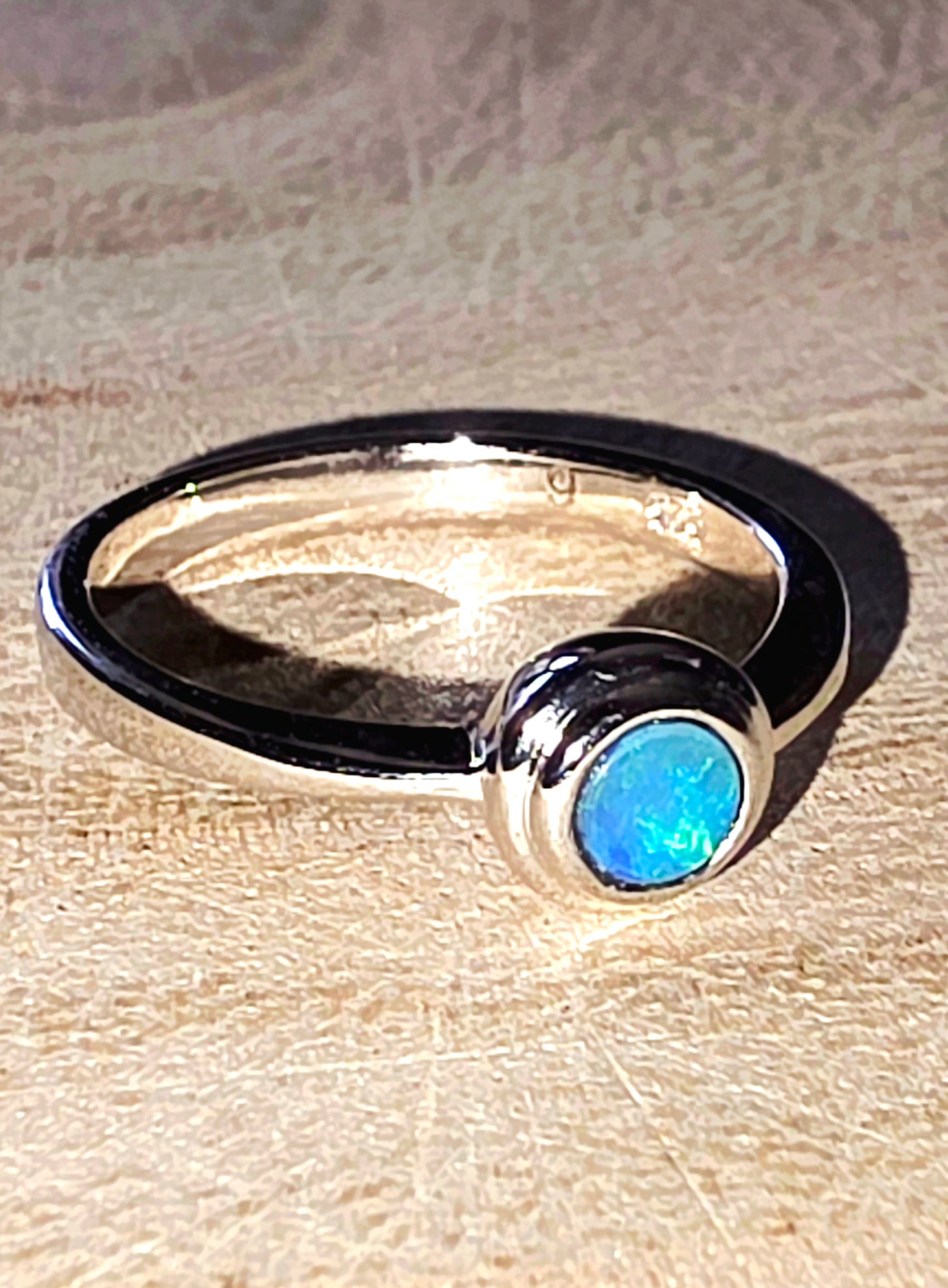 Silver ring with a blue opal stone on a wooden surface
