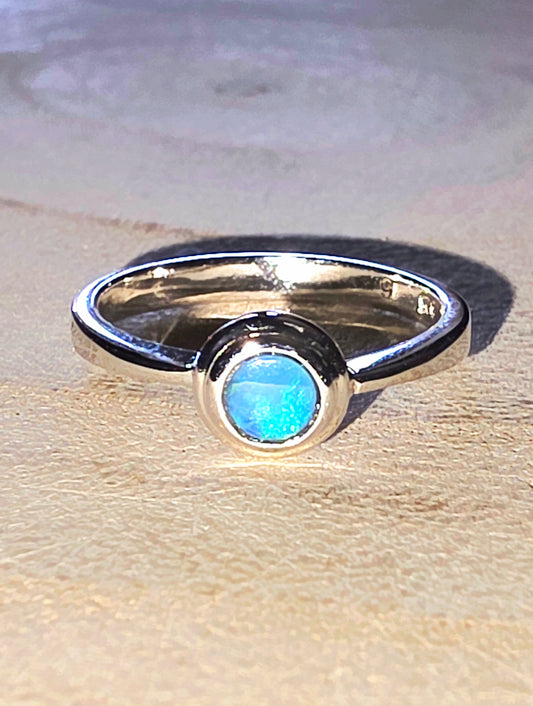Silver ring with a blue opal on a wooden surface