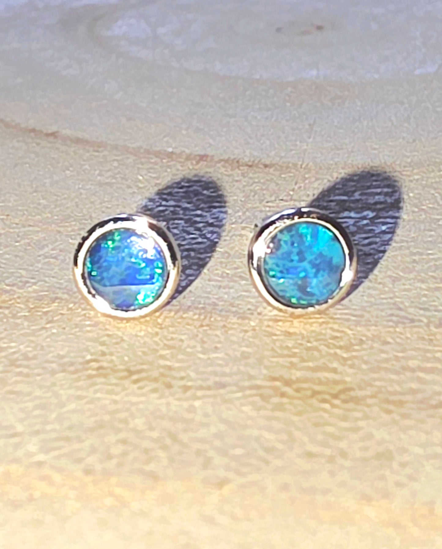 Pair of blue opal stud earrings on a light wood background