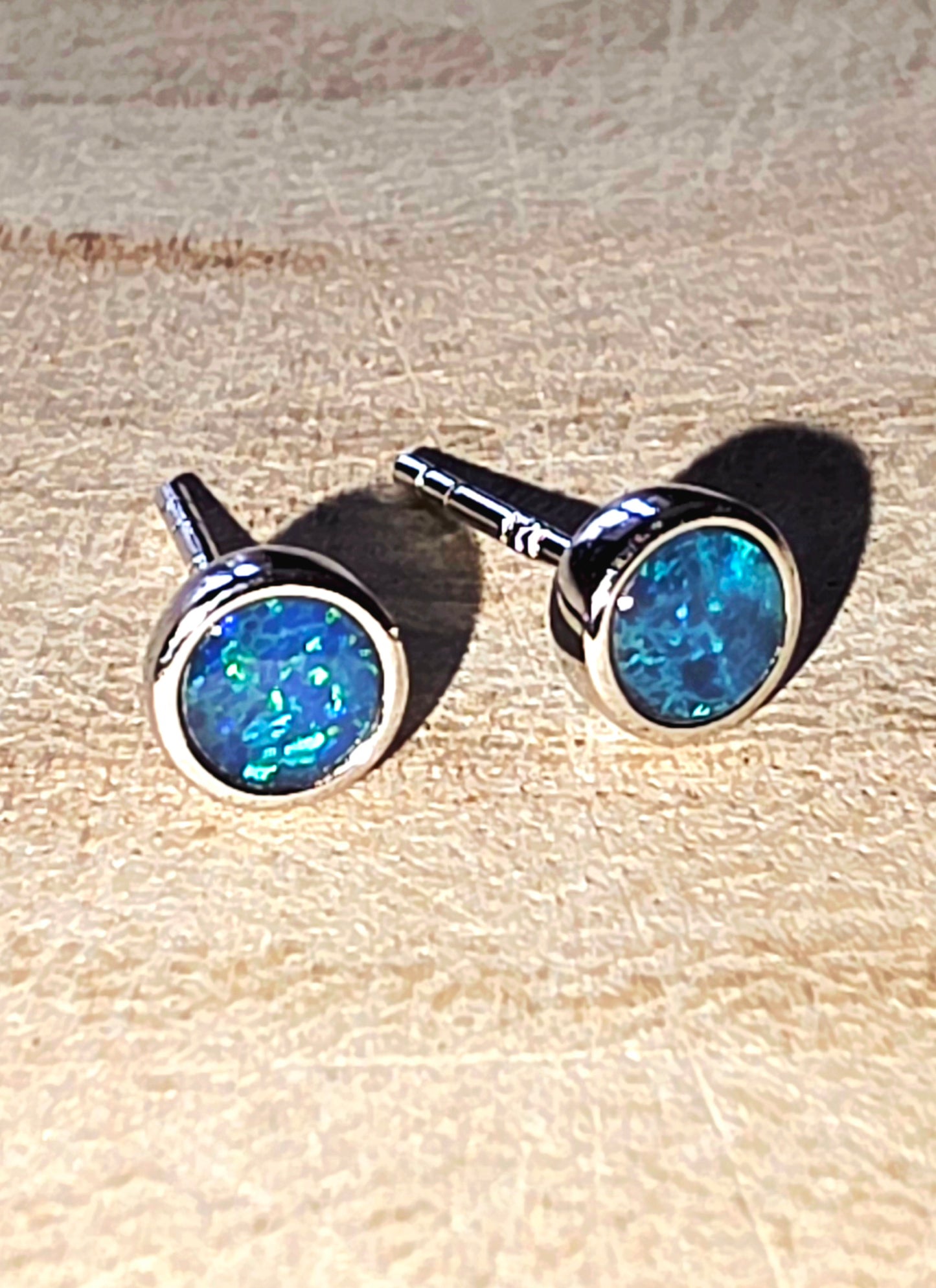 Pair of blue opal stud earrings on a light wood background