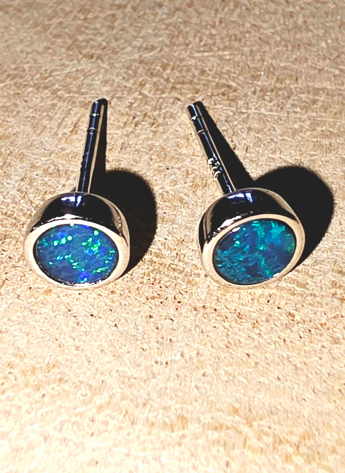 Pair of opal stud earrings on a beige surface