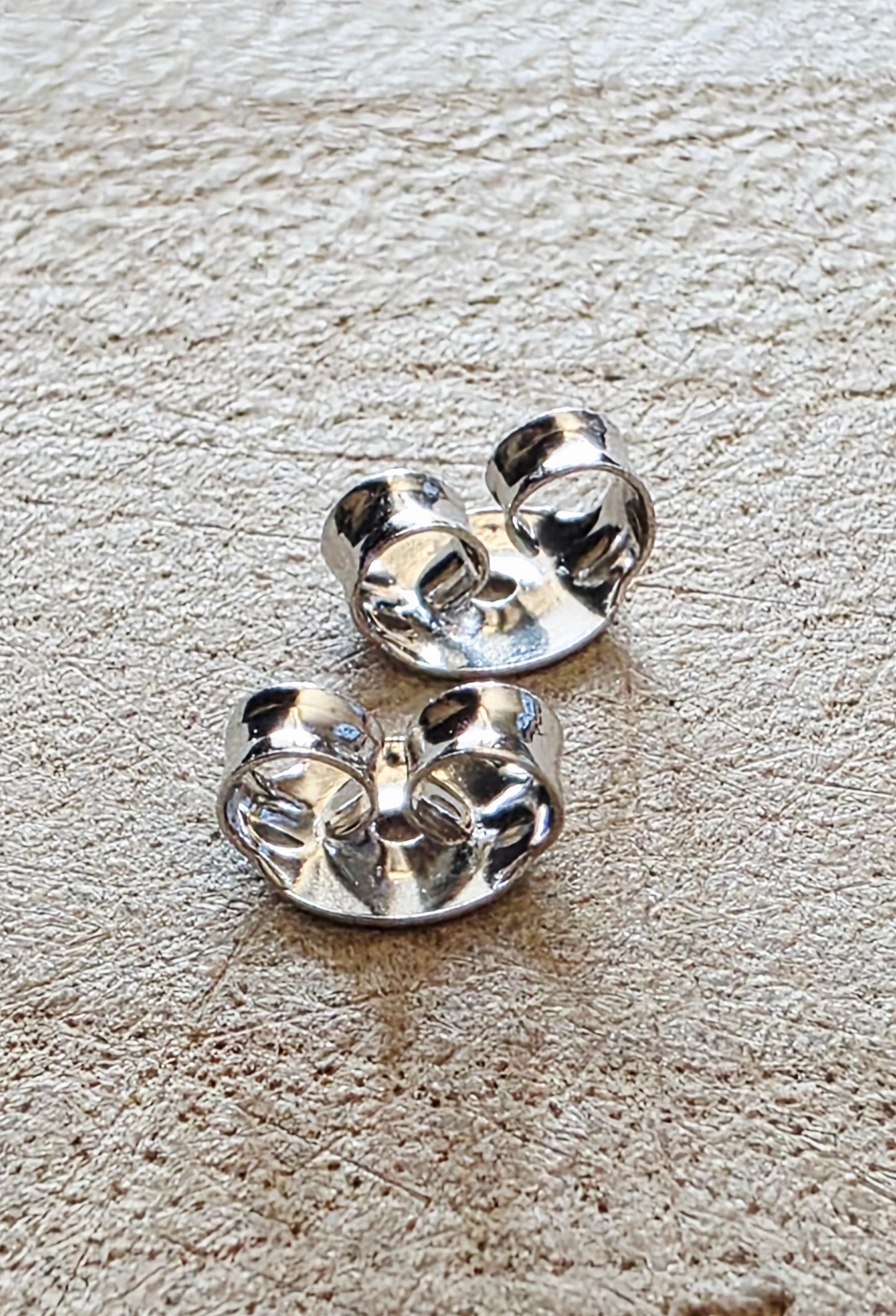 Pair of silver earring butterfly backs on a textured beige surface