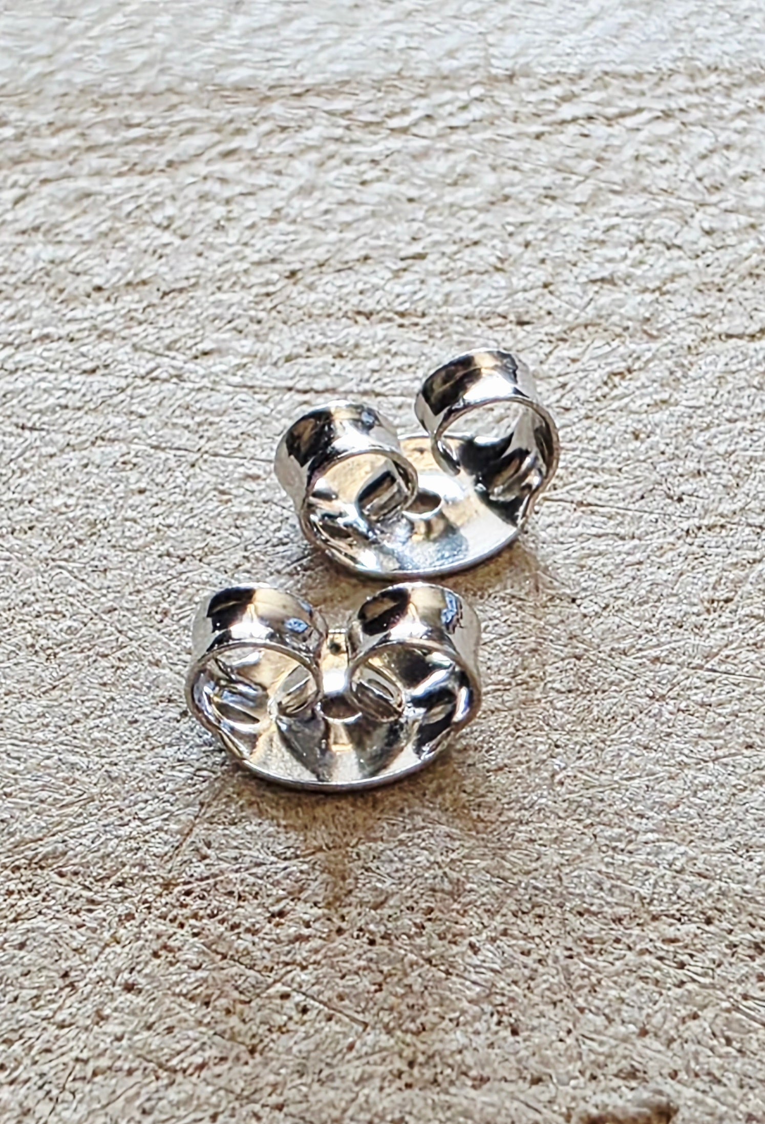 Pair of silver earring butterfly backs on a textured beige surface