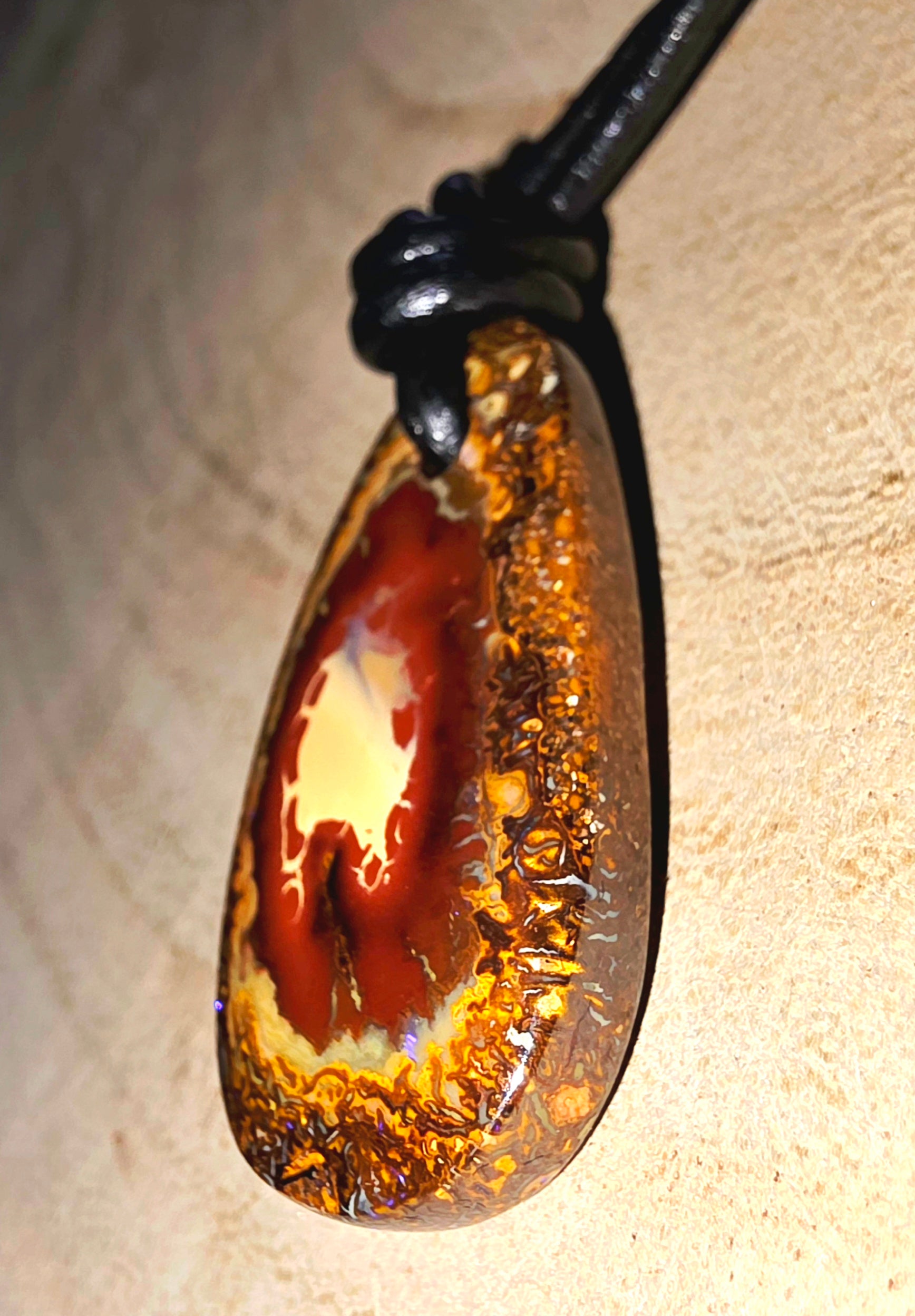 Teardrop-shaped pendant with brown and gold colours on a beige background