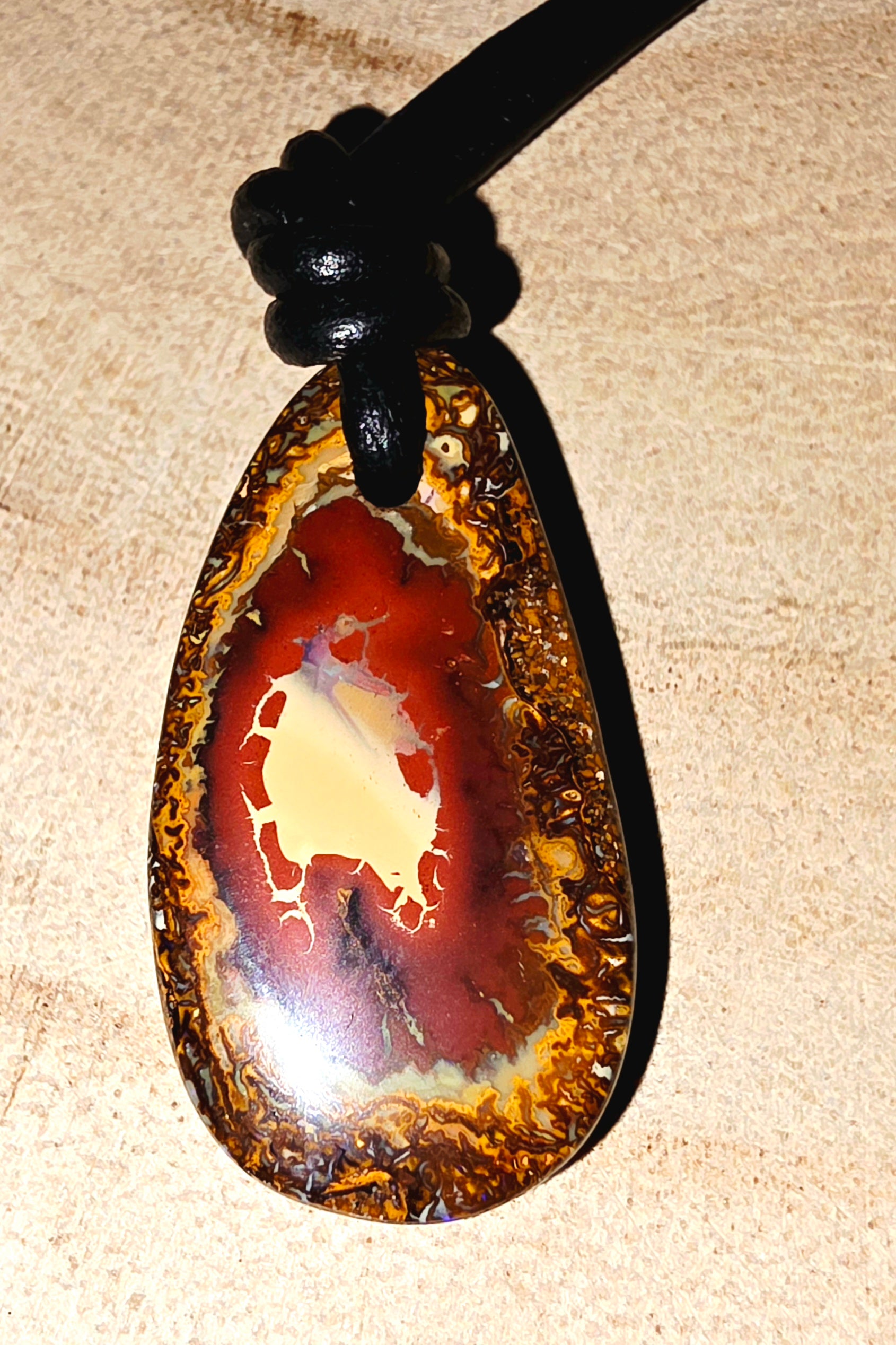 Teardrop-shaped boulder opal pendant on a beige background