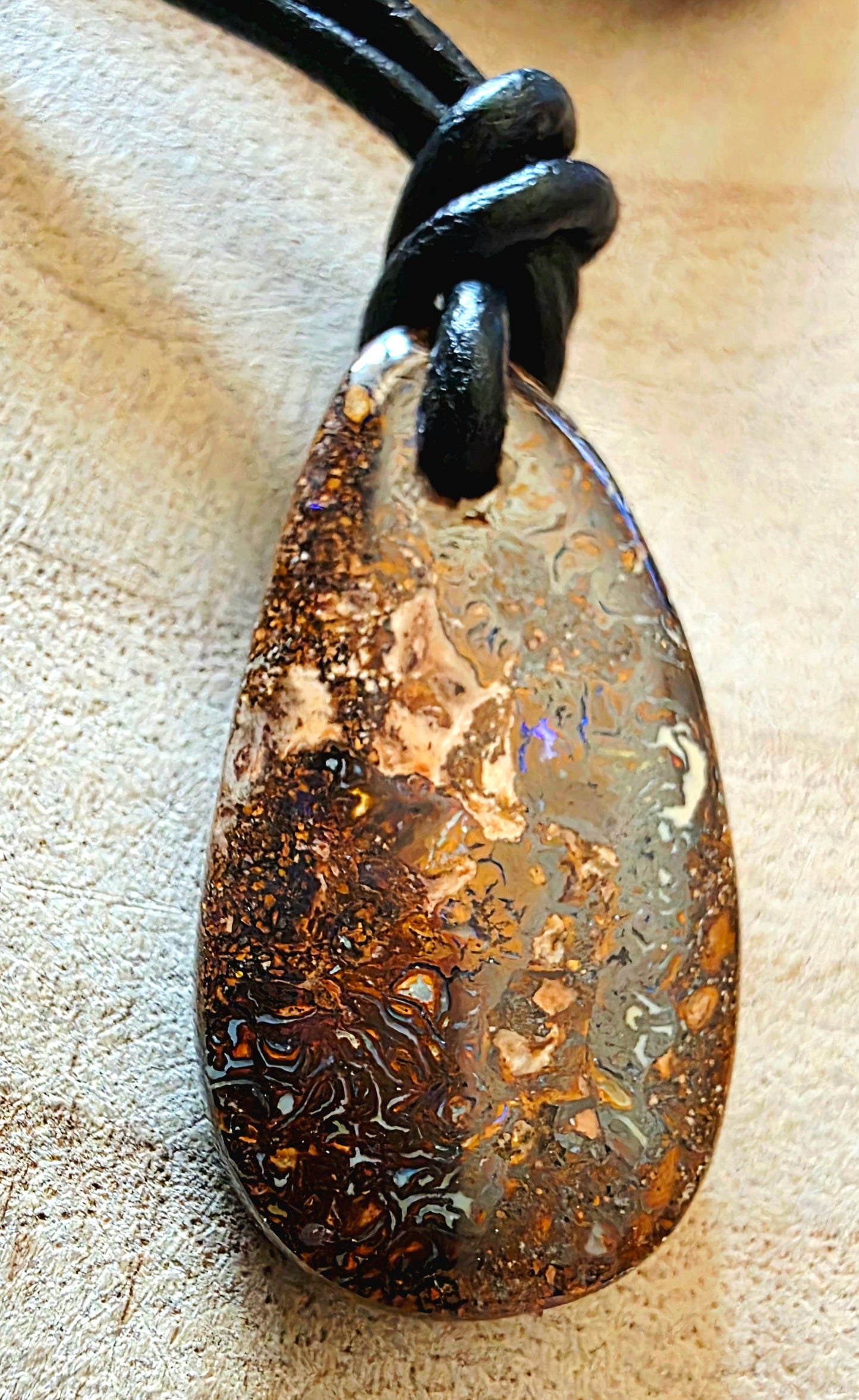 Teardrop-shaped pendant with a textured surface on a black cord against a beige background