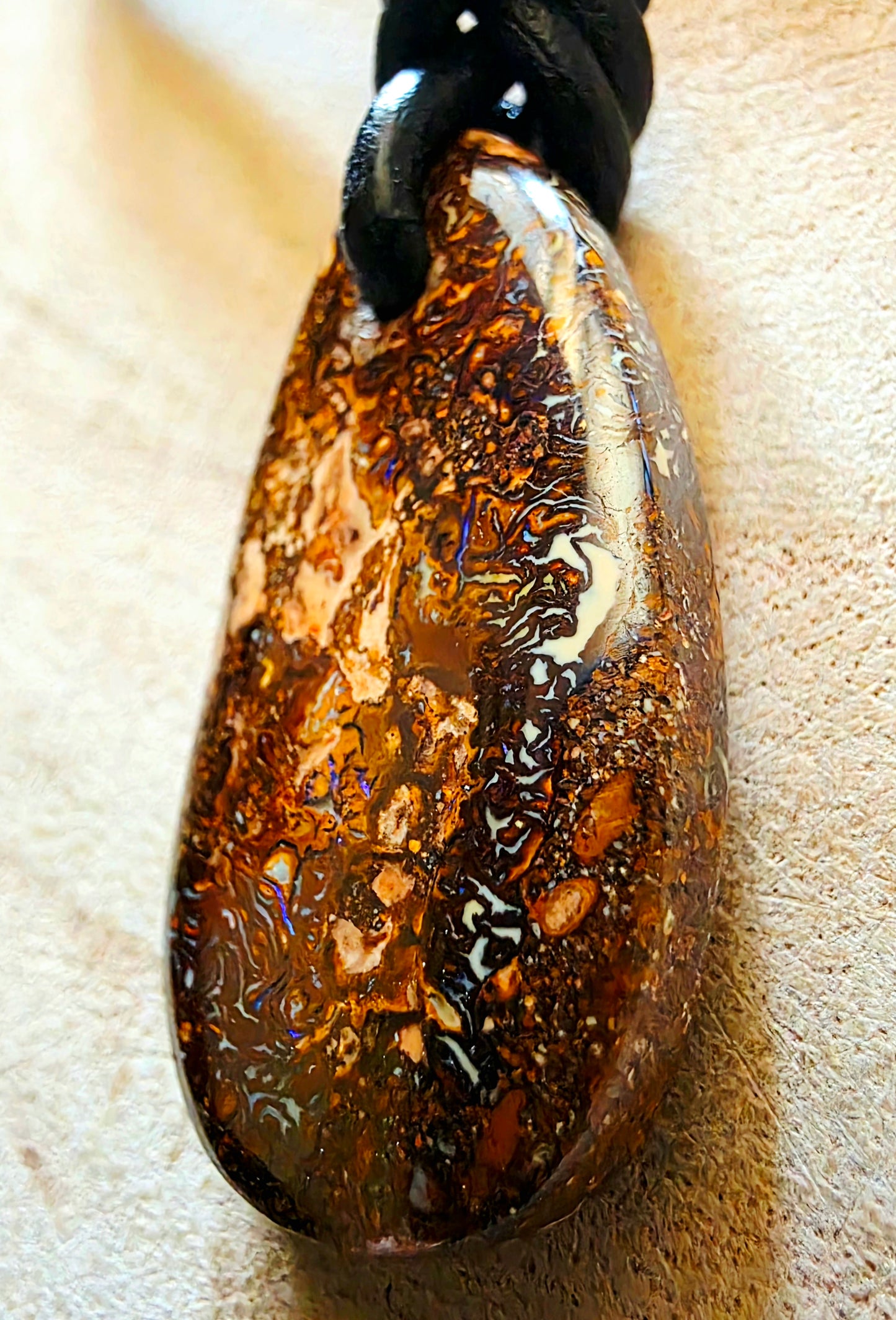 Teardrop-shaped opal pendant on a beige background