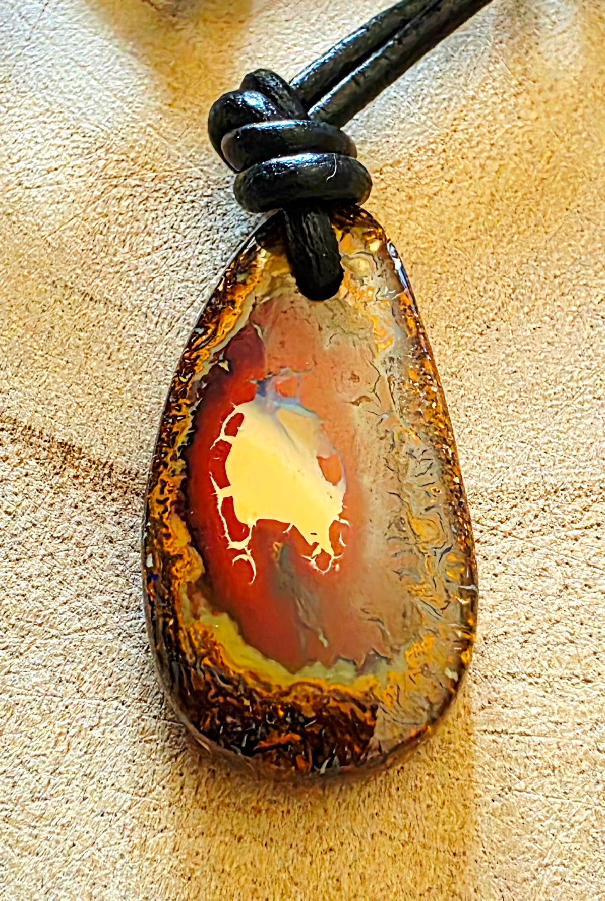 Teardrop-shaped opal pendant on a leather cord against a beige background