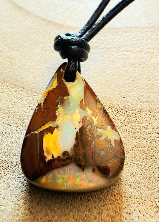 Opal pendant on a black cord against a beige background